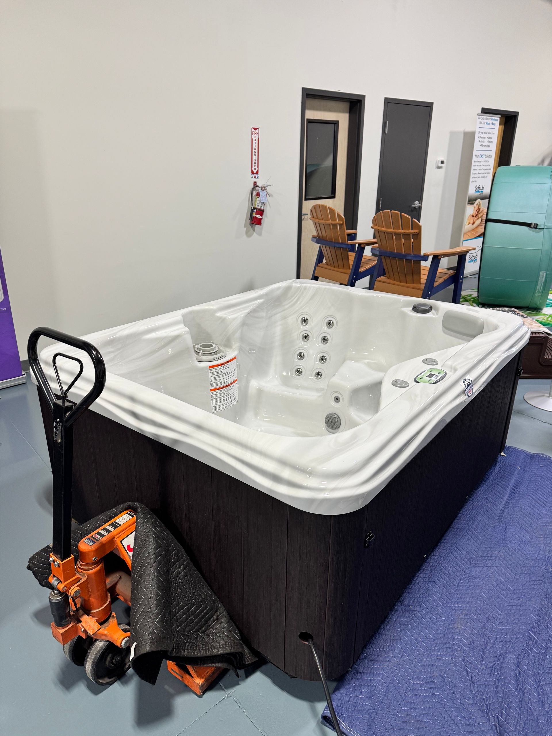 Hot tub in a showroom setting, with an orange pallet jack and blue moving blanket.