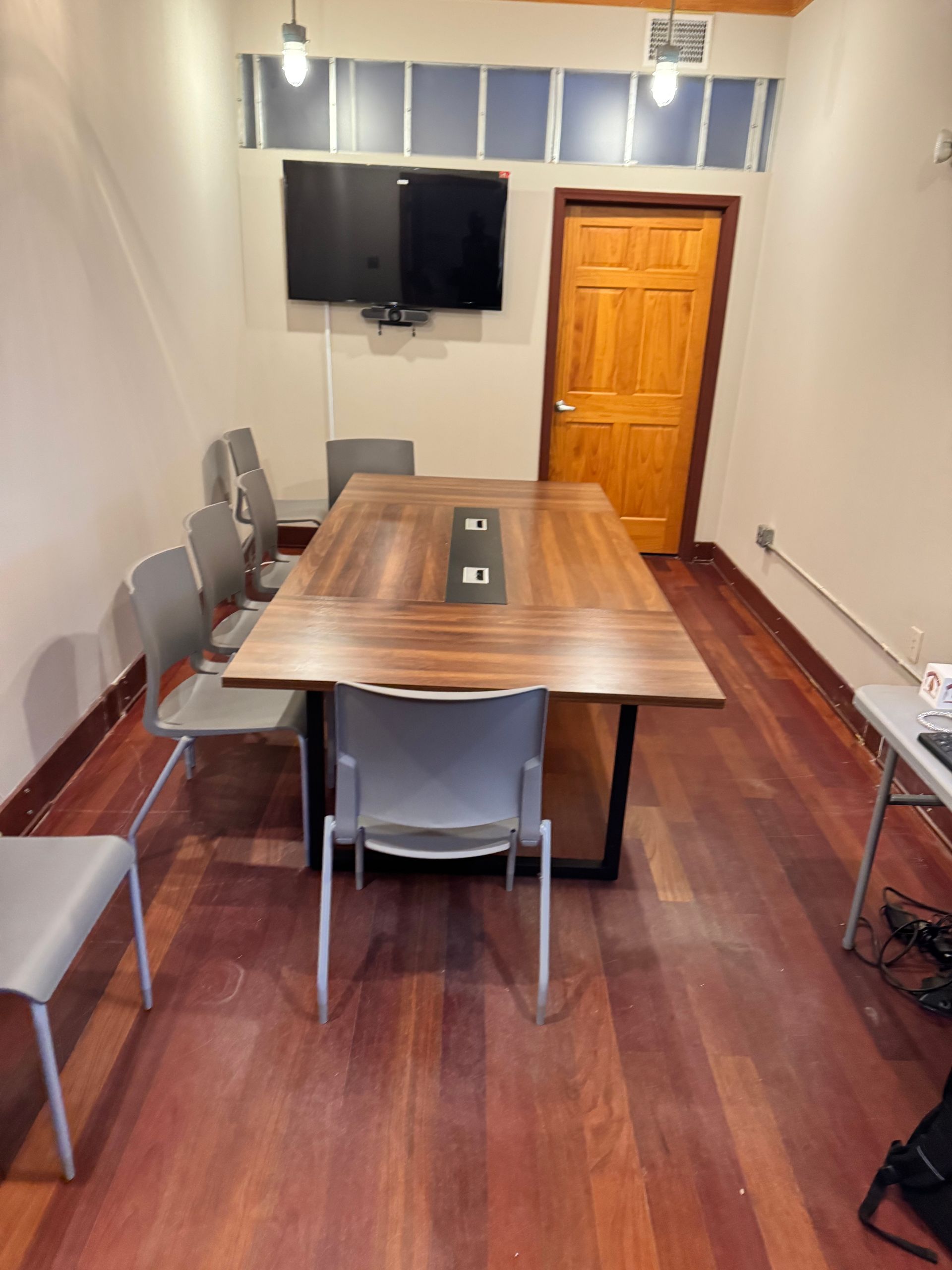 Conference room with wooden table, chairs, TV, door, and hardwood floor.