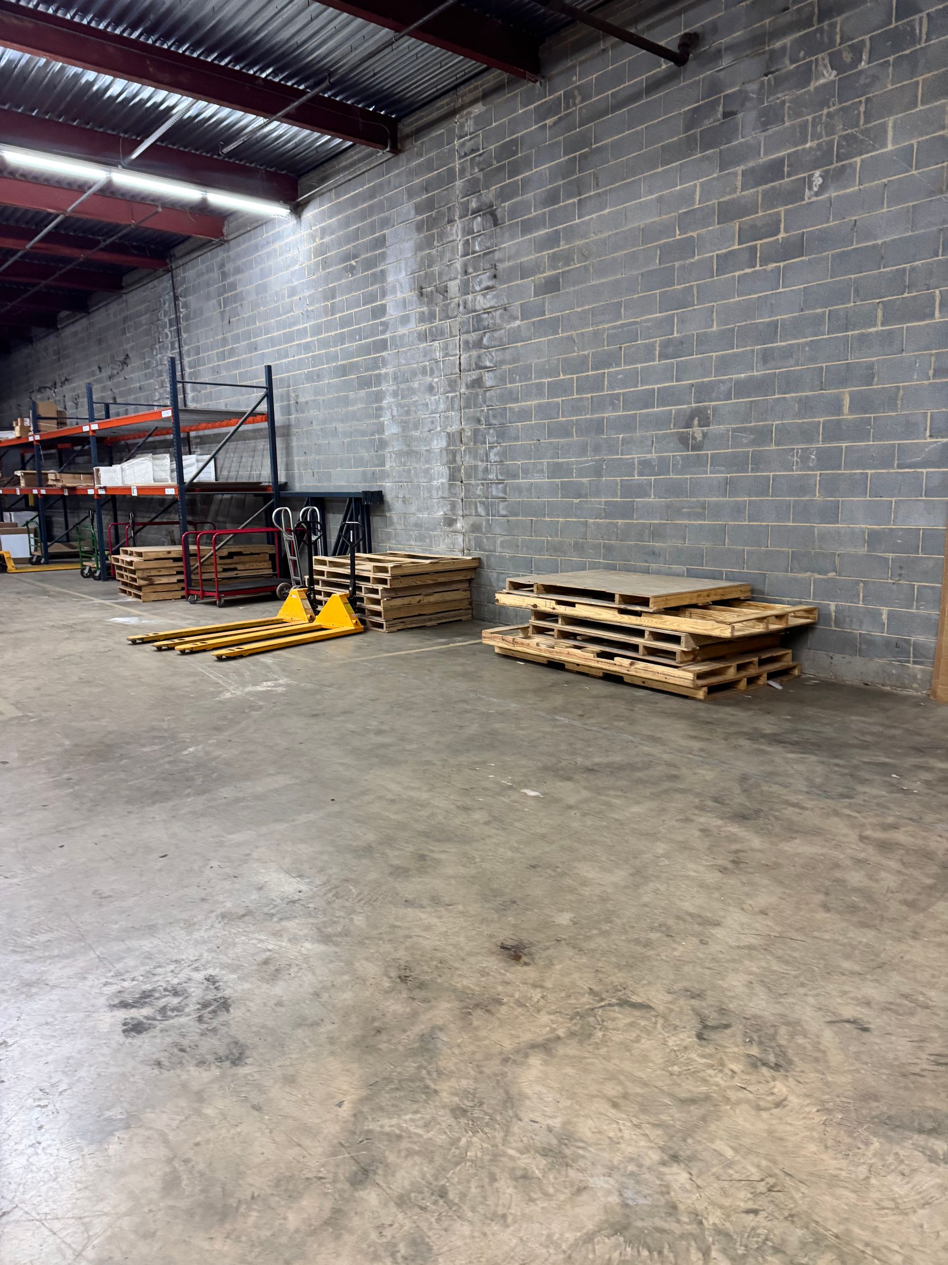 Warehouse interior with stacked wooden pallets and concrete block walls.