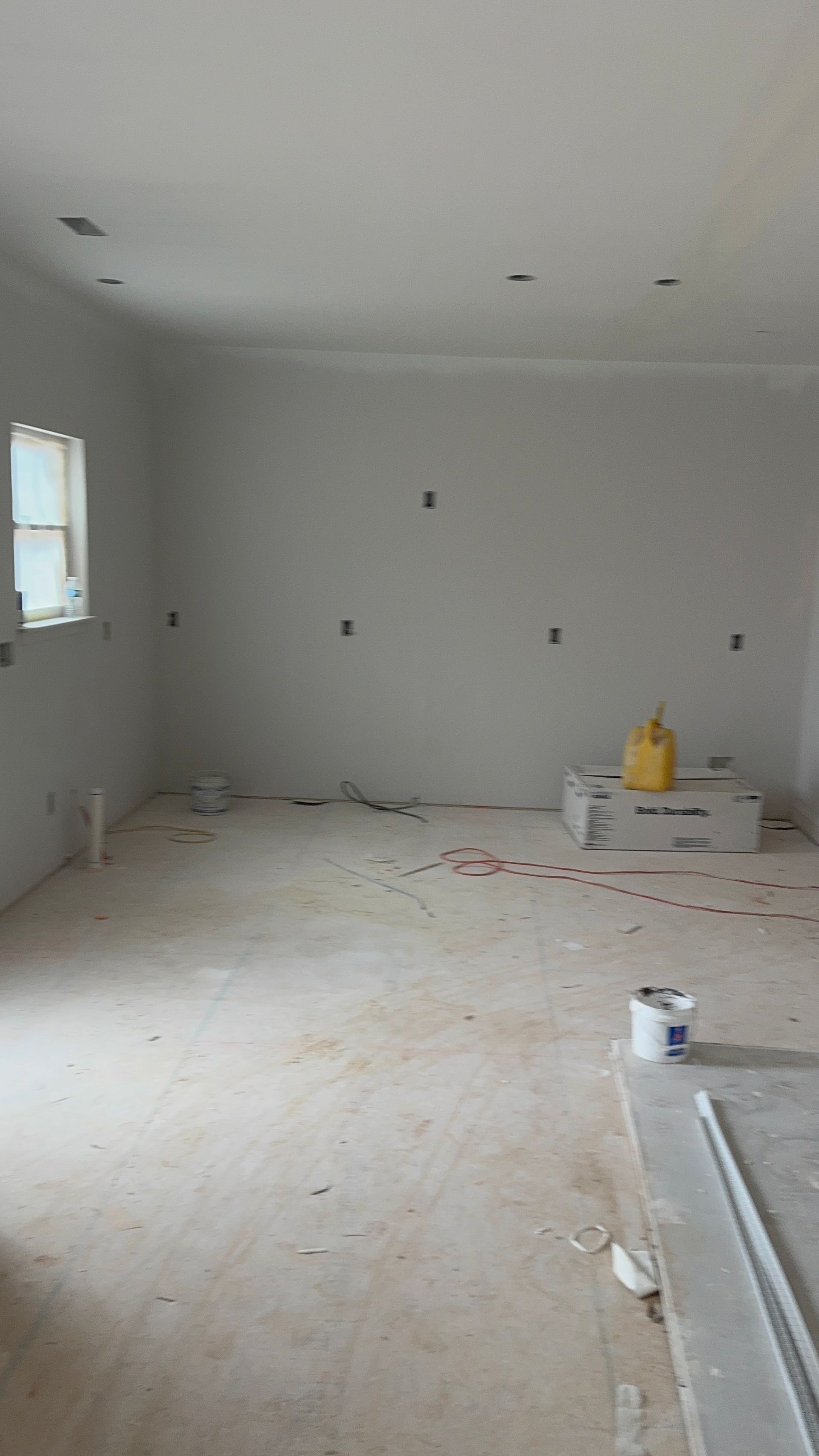 Unfinished room with drywall, electrical outlets, and exposed wires. Construction debris and a paint can are visible.