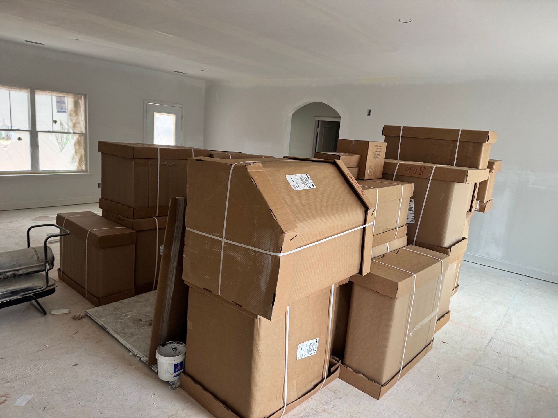 A stack of large cardboard boxes in a room under construction with white walls.