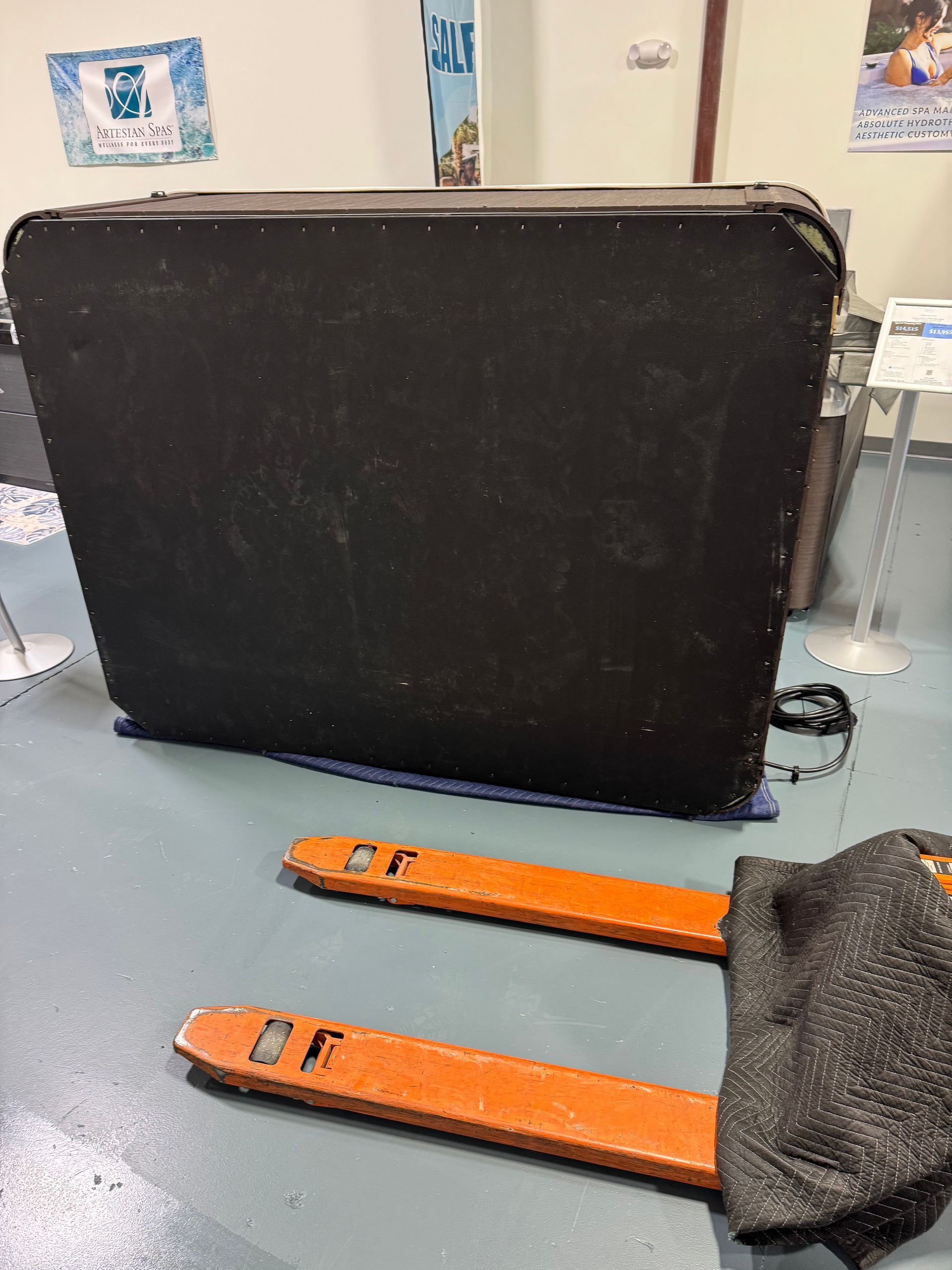 A black box on a pallet jack, orange forks. Indoors with signs in background.