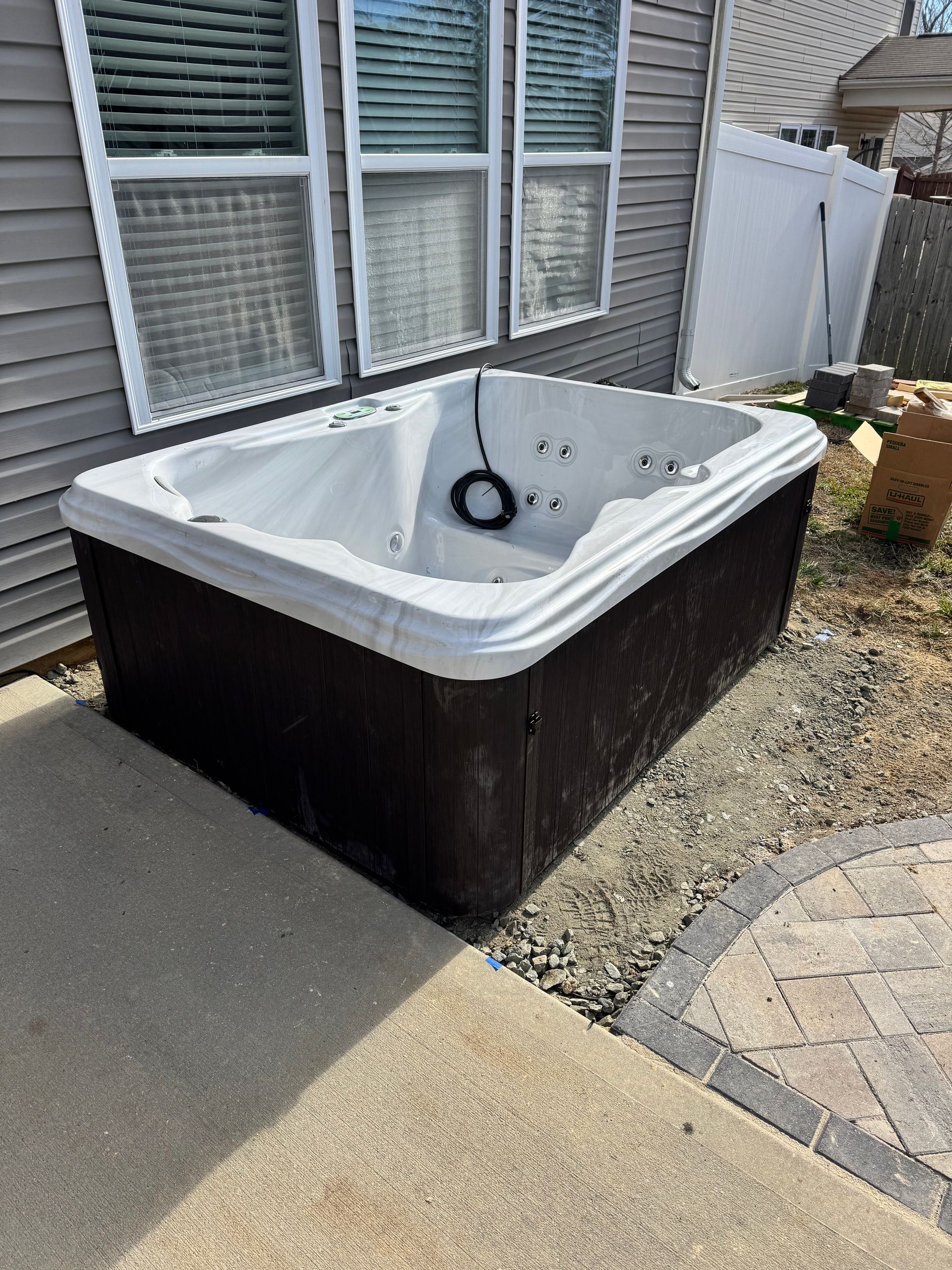 Hot tub outside, rectangular, brown and white, near house with windows and gray siding, on gravel.