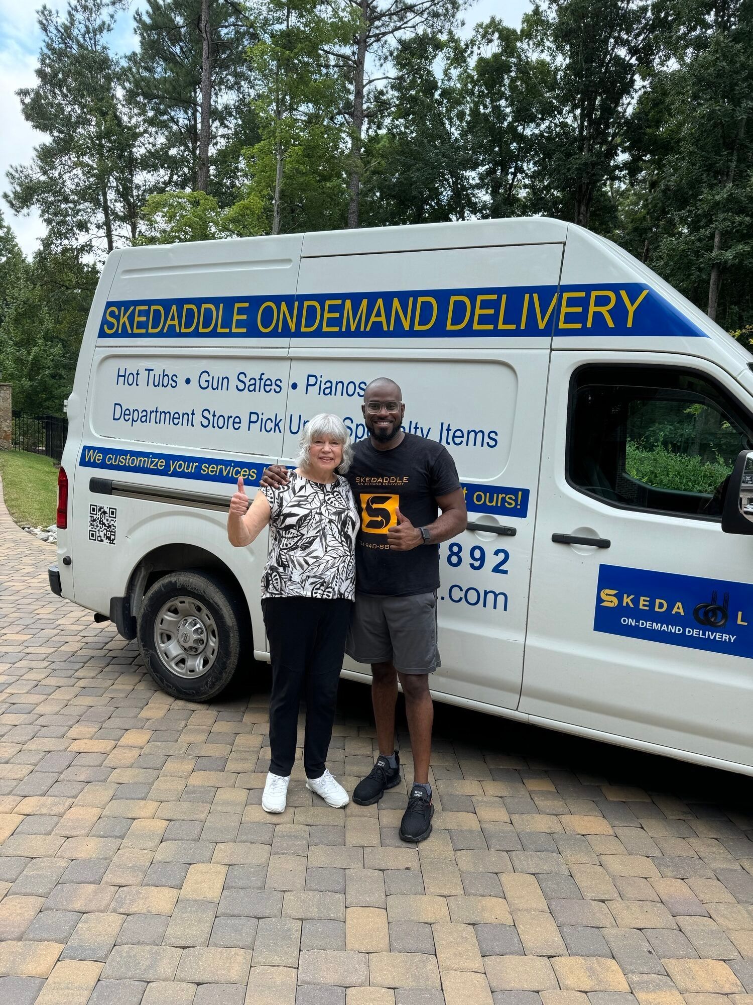 A woman and a man pose with a delivery van. The van has business logos and text.