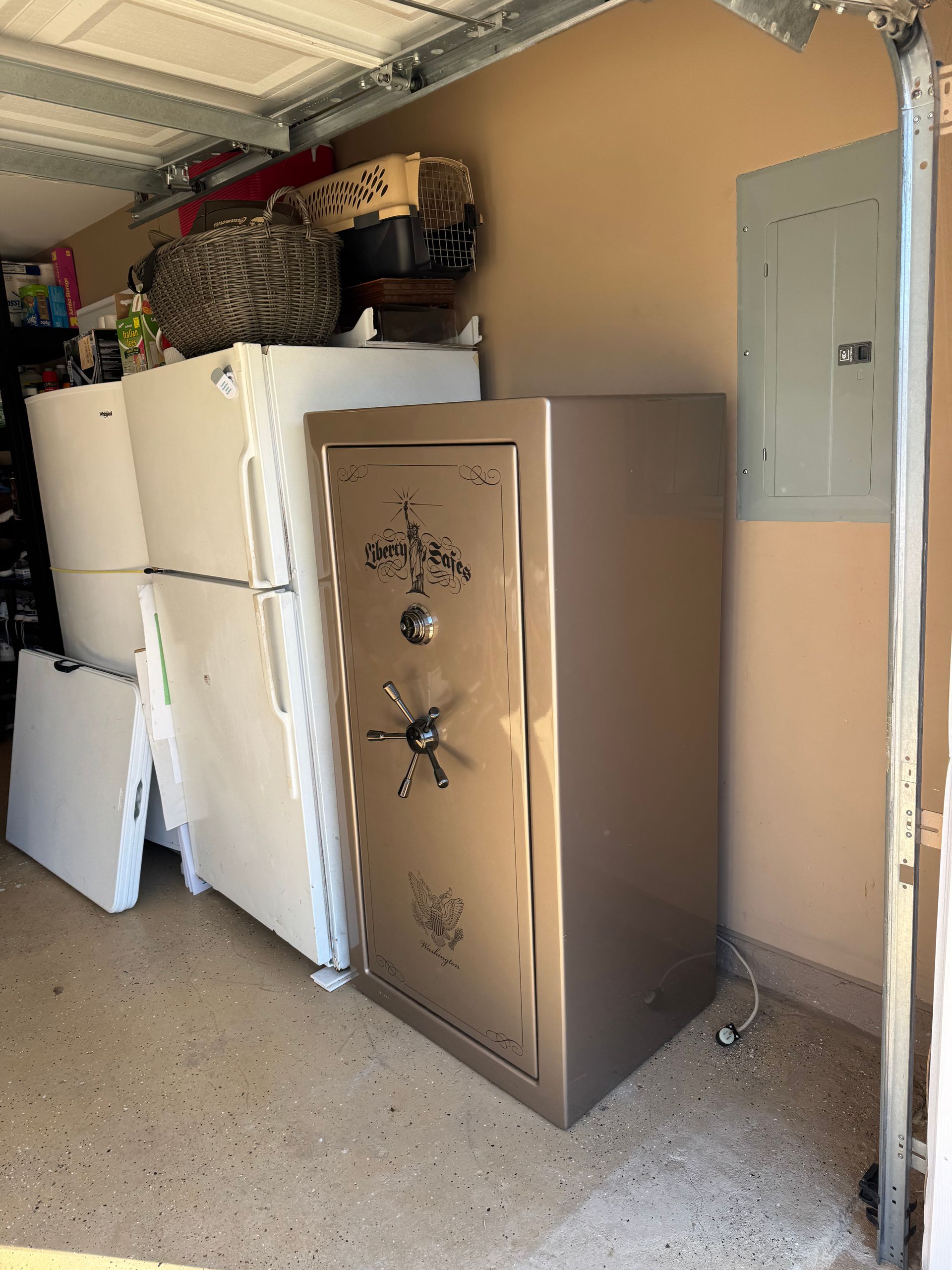 A large safe and a refrigerator sit in a garage, next to an electrical panel.