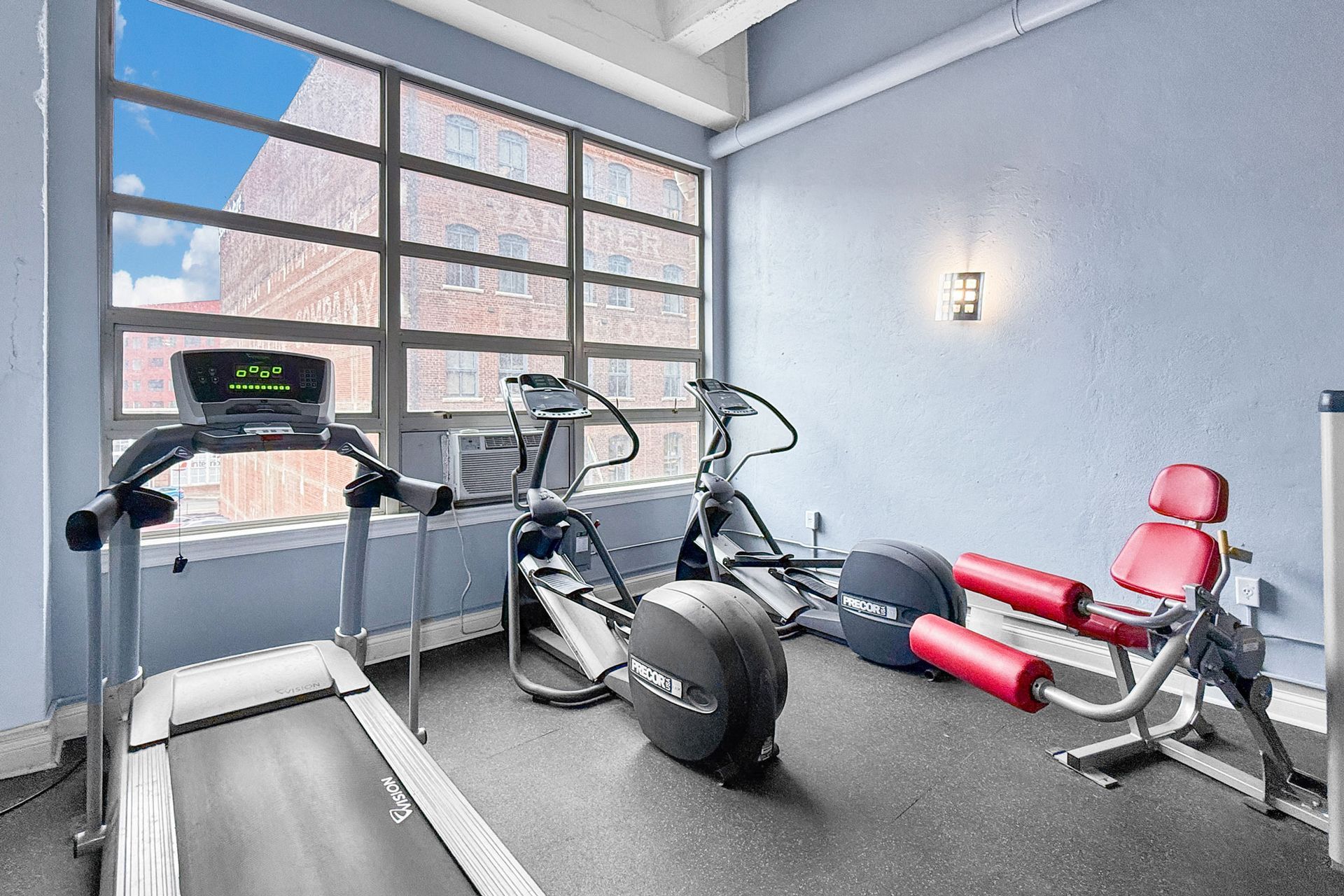 A small home gym with a treadmill, two elliptical machines, and a leg curl machine near a large window.