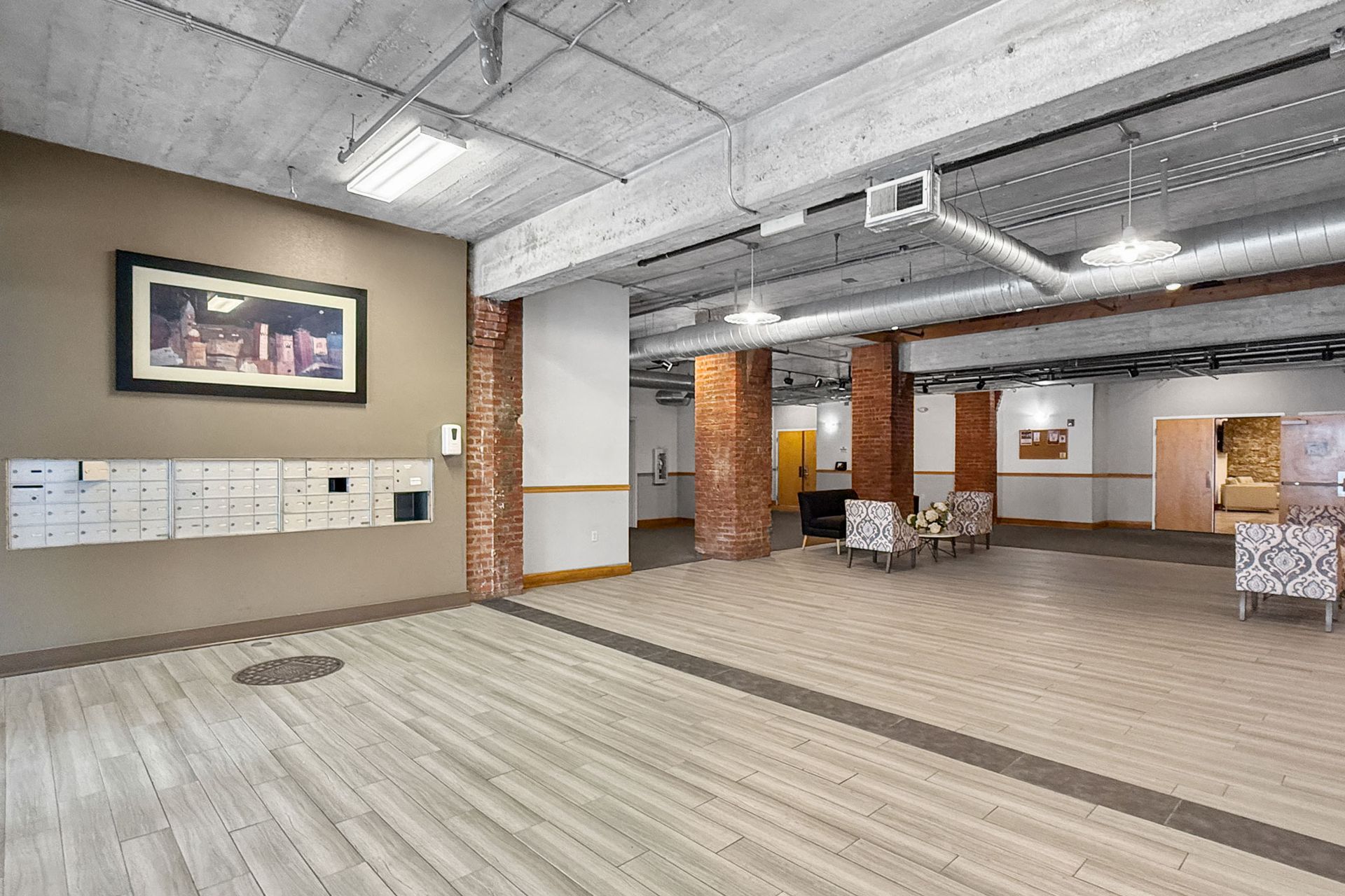 Modern lobby featuring mailboxes on a tan wall, exposed brick columns, concrete ceilings, and casual seating area.
