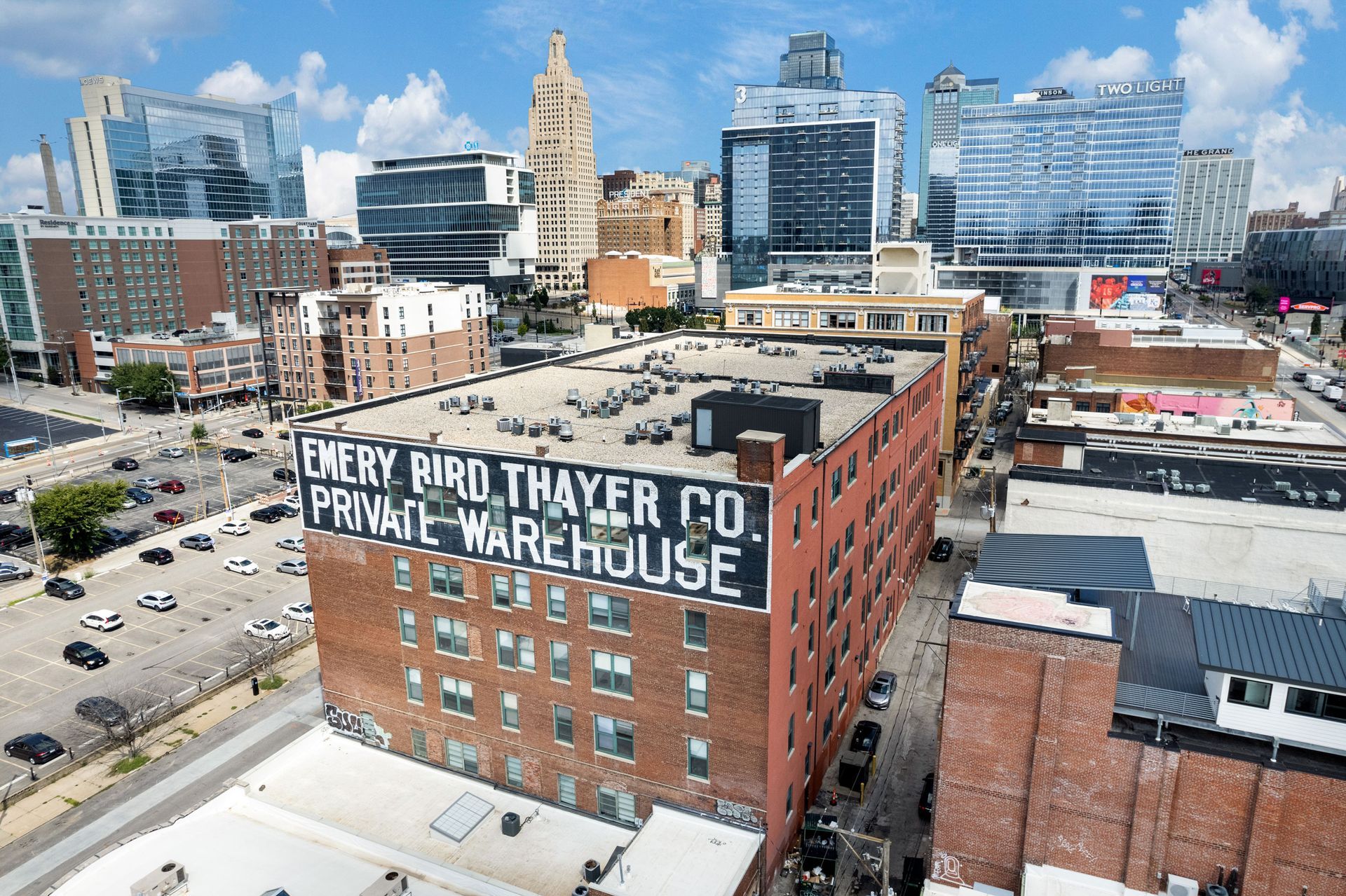 An aerial view of the brick Emery, Bird, Thayer Co. warehouse building in a dense city setting with skyscrapers nearby.