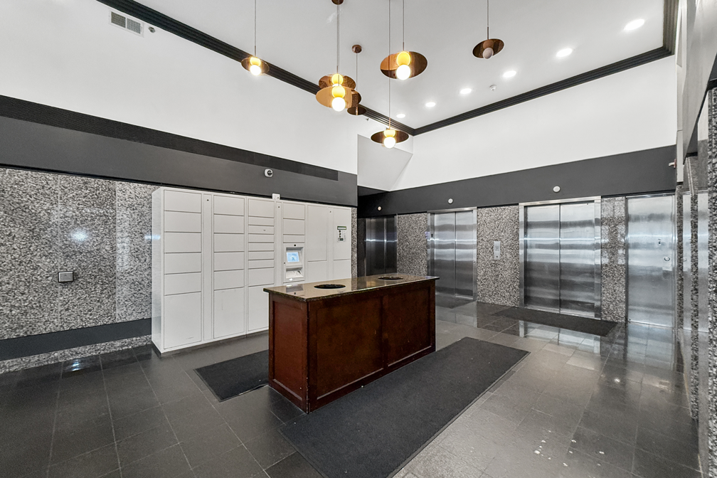 A modern apartment building lobby with gray marble walls, dark tiled floors, elevators, and a wooden concierge desk.