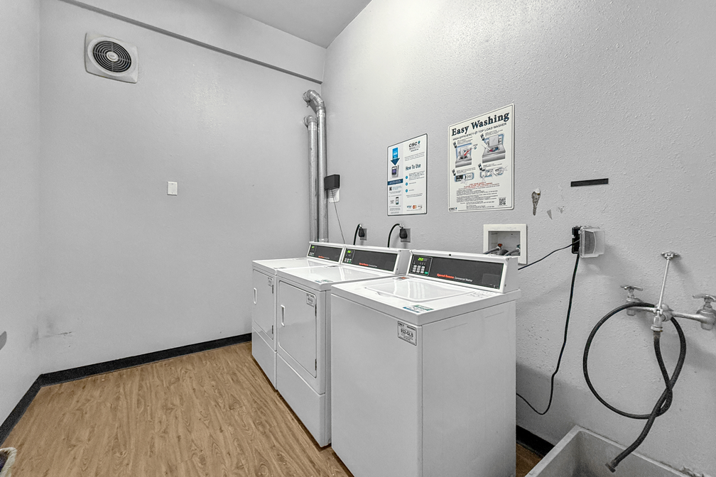 A small laundry room with a white washer and dryer, light wood-style flooring, and wall-mounted instructional signs.