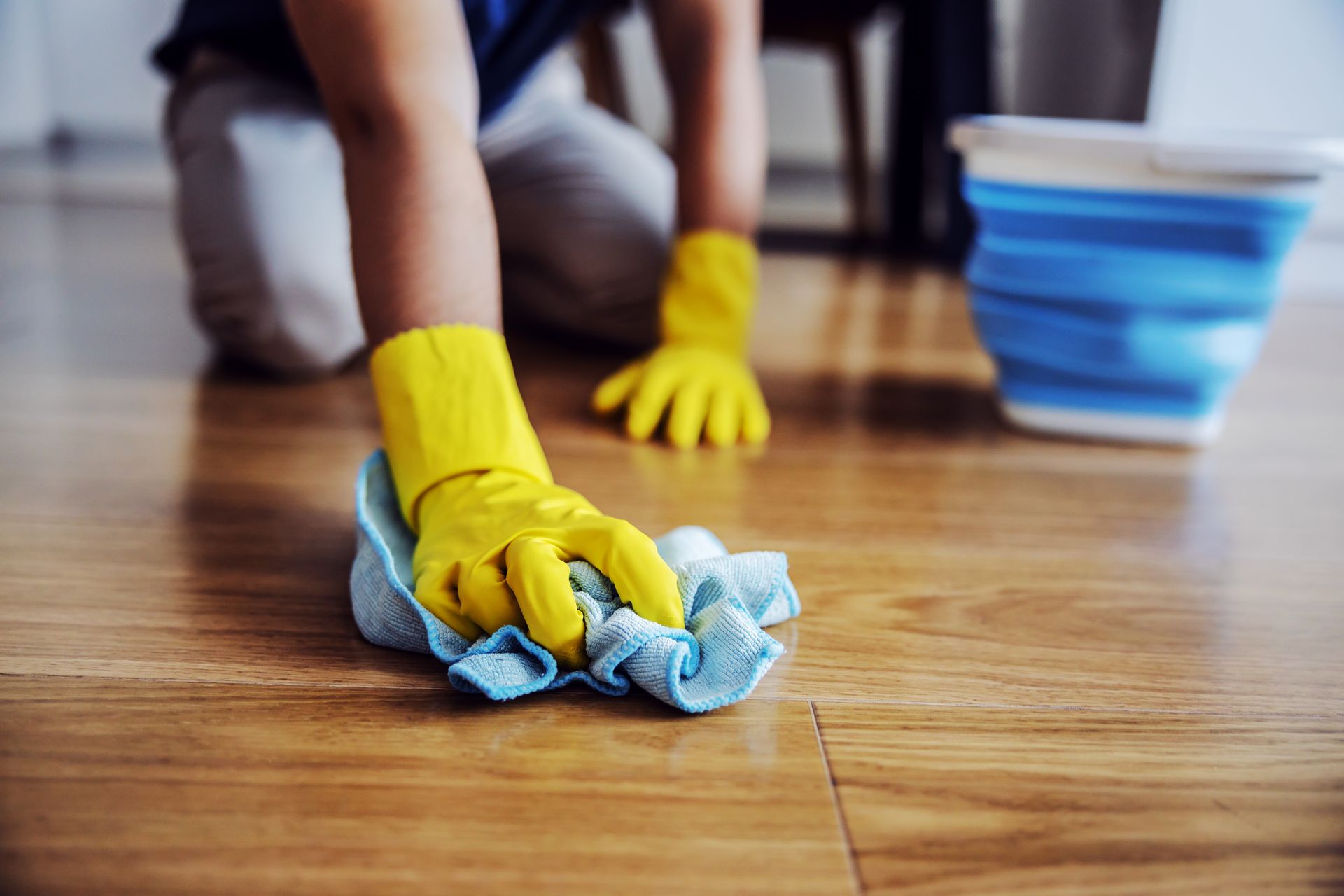 A person wearing yellow gloves is cleaning a wooden floor with a cloth.