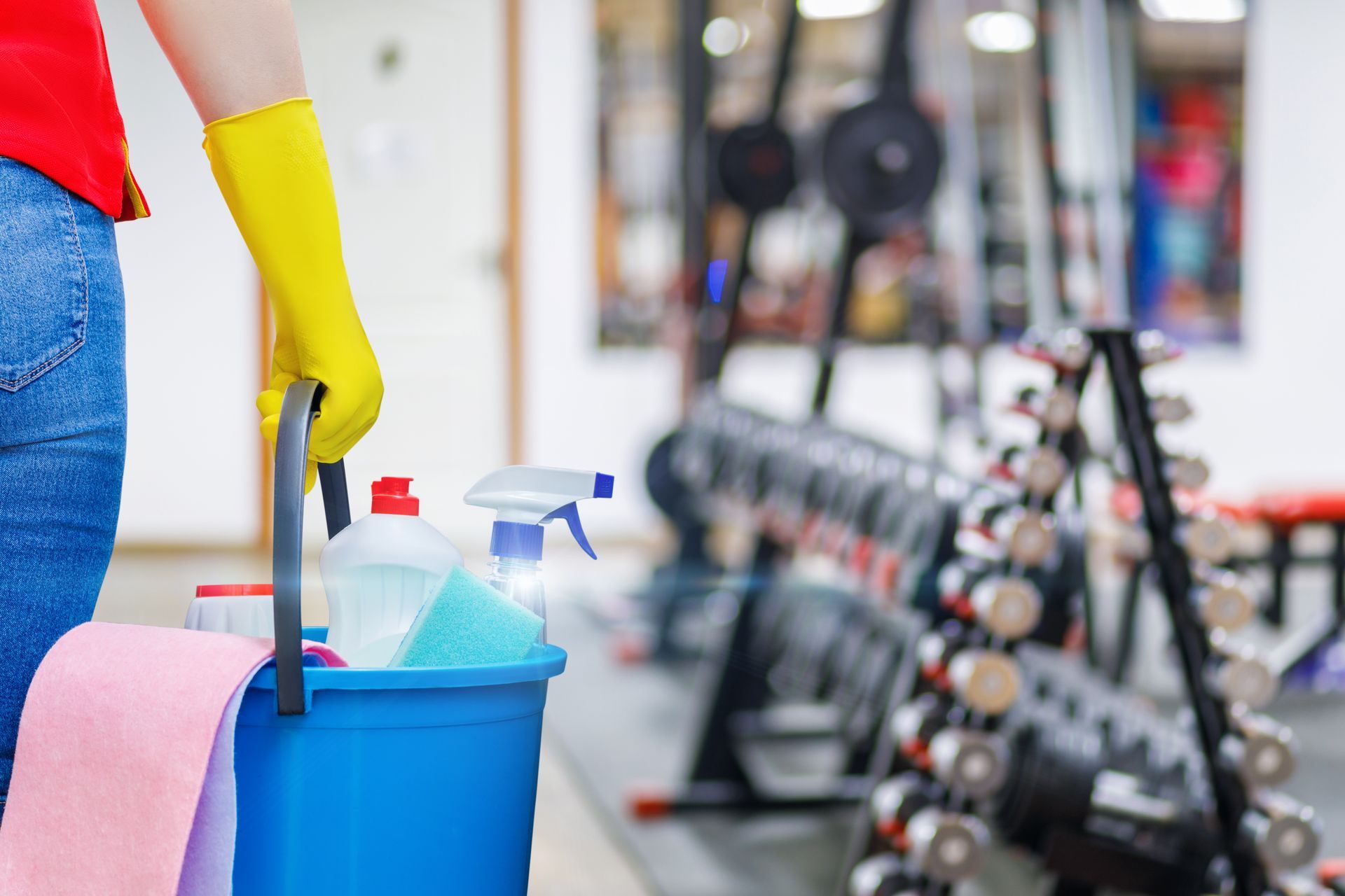 A woman is cleaning a gym with a mop and bucket.