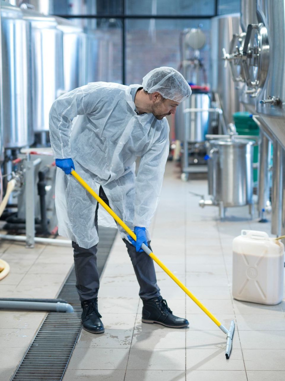 A man is cleaning the floor of a factory with a mop.