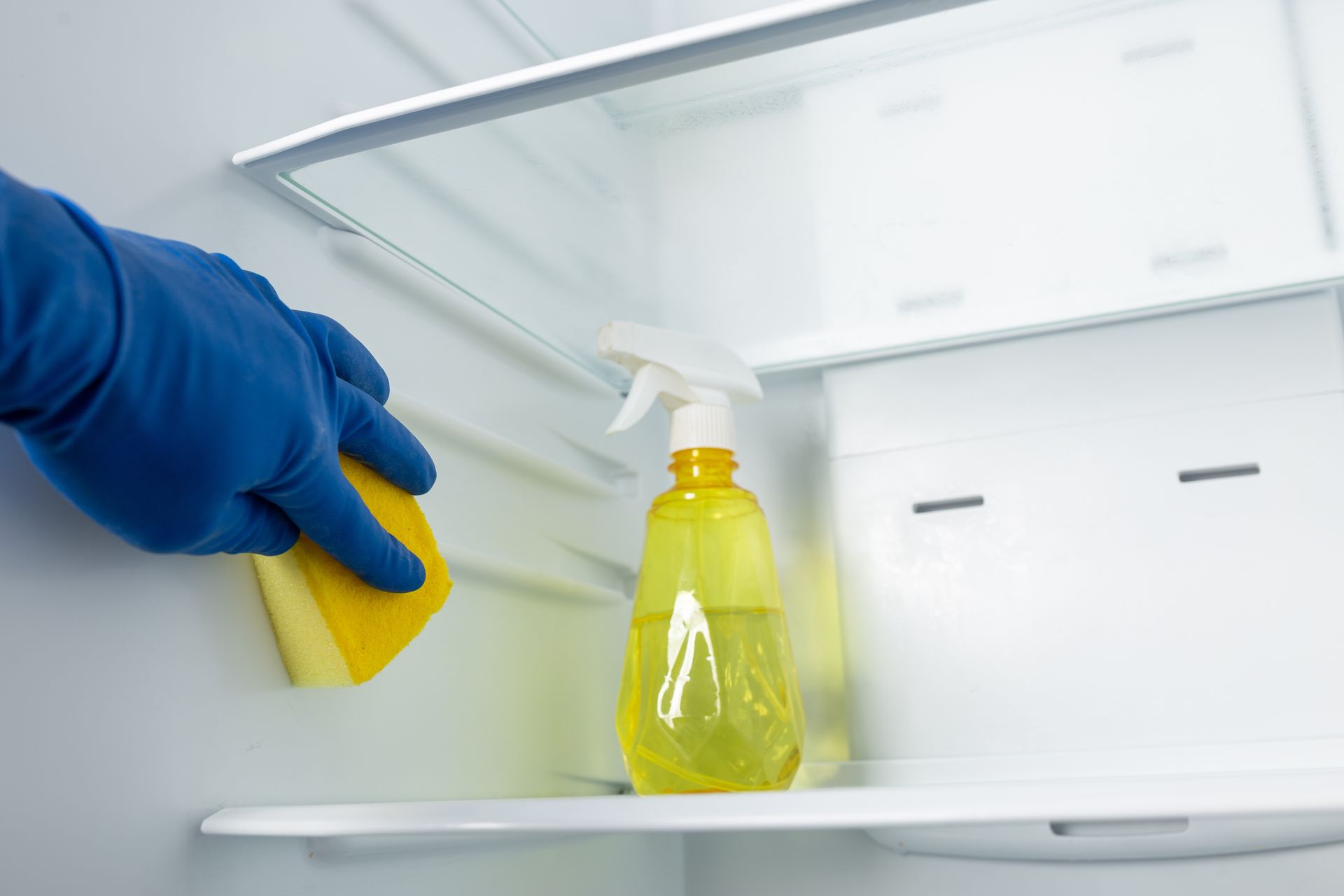 A person is cleaning a refrigerator with a sponge and spray.