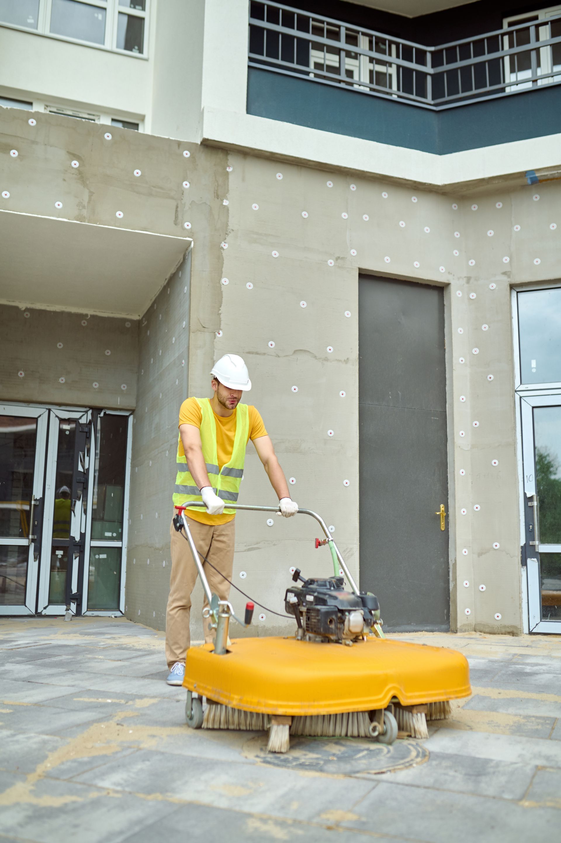 A construction worker is using a machine to clean the sidewalk in front of a building.