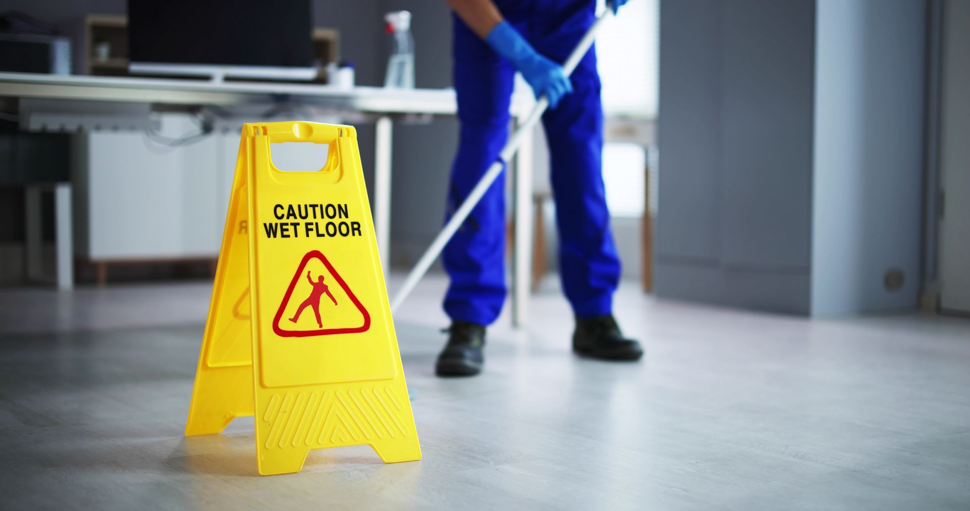 A man is mopping the floor next to a caution wet floor sign.