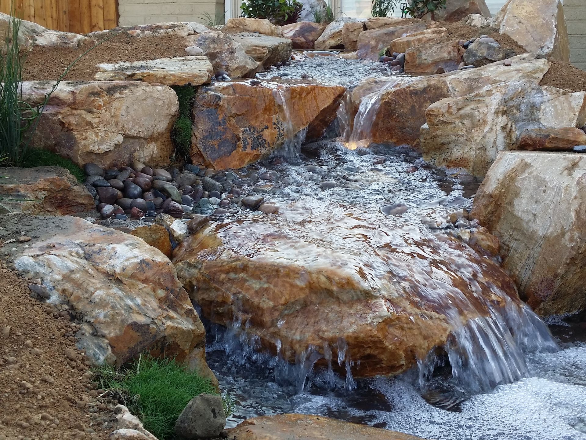Waterfall cascading over large, brown rocks, with clear water and some vegetation.