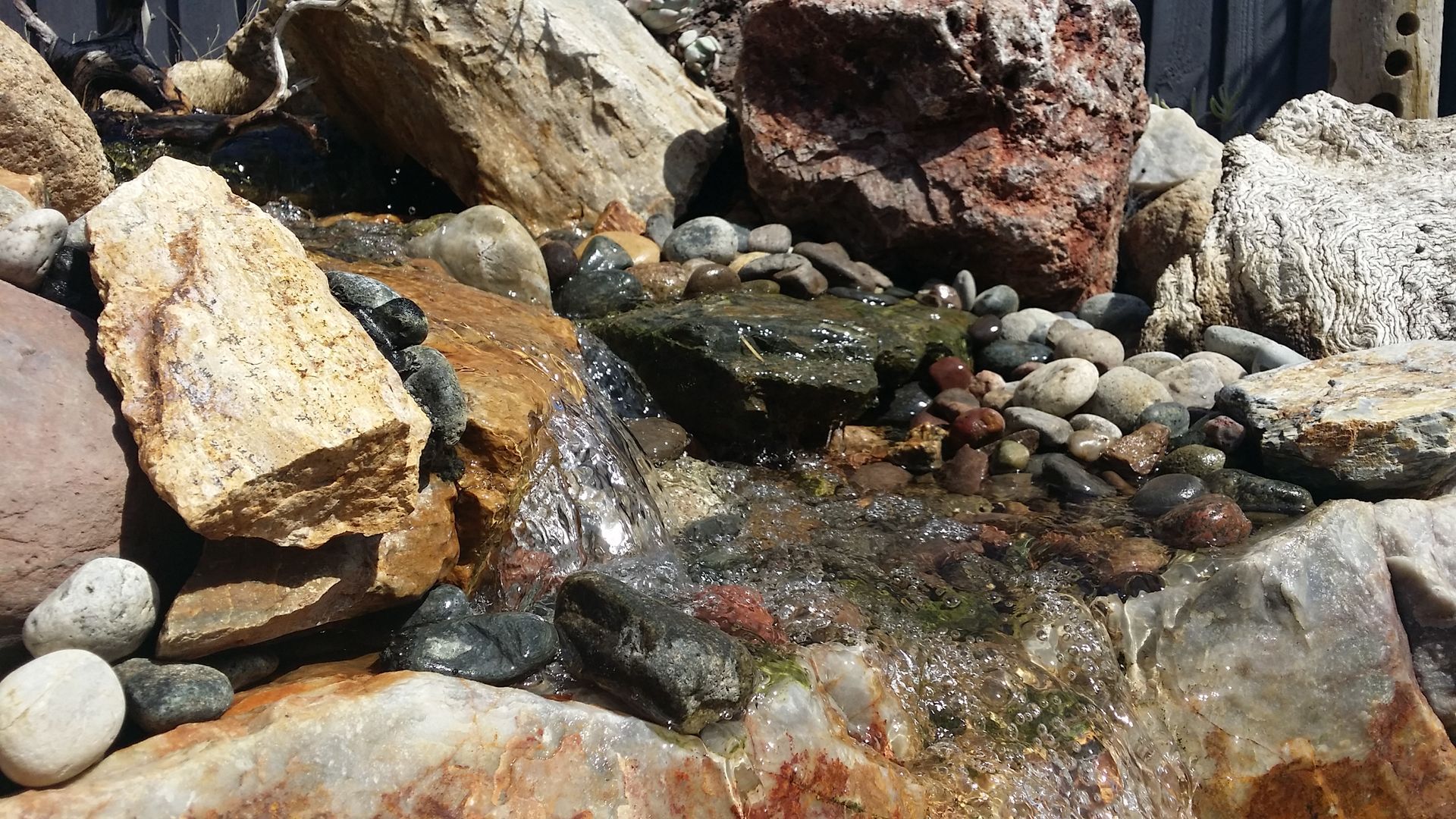 Water cascading over rocks in a naturalistic garden setting with various colored stones.