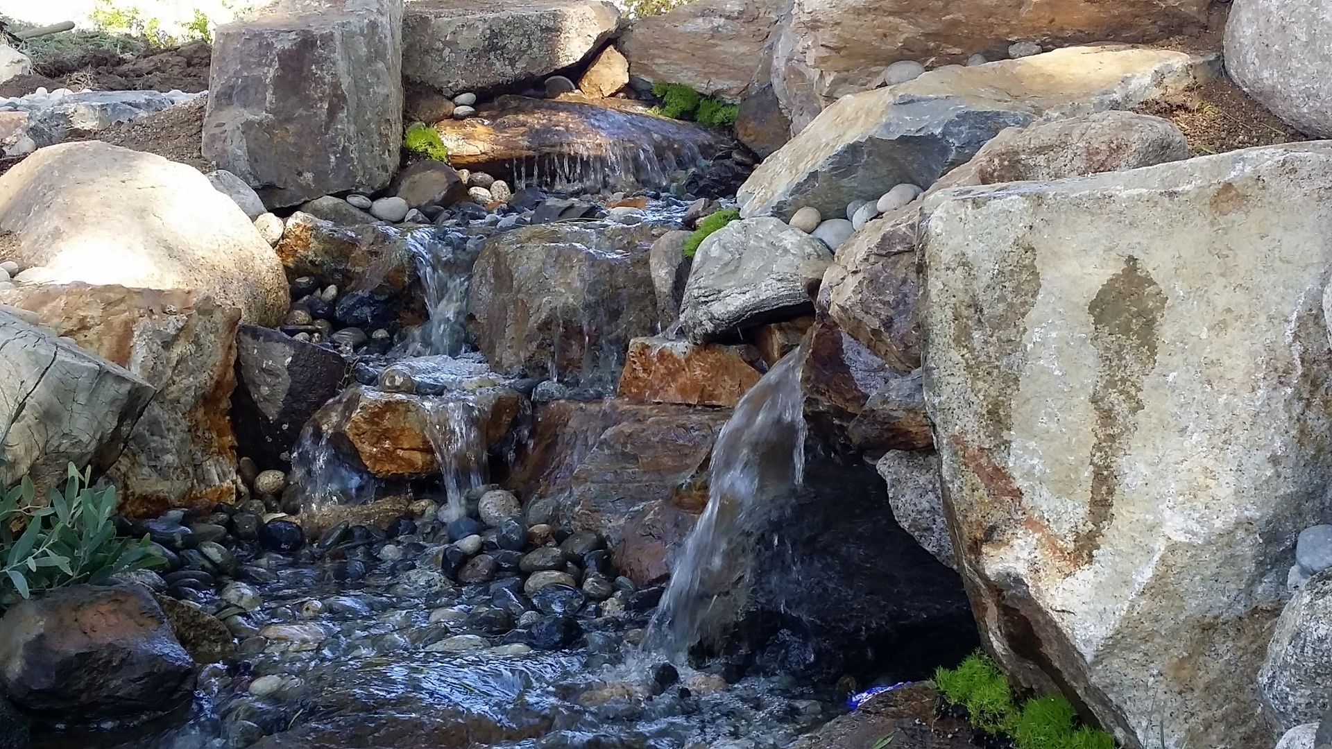 Waterfall cascading over rocks in an outdoor setting; water sparkles, flowing among stones.