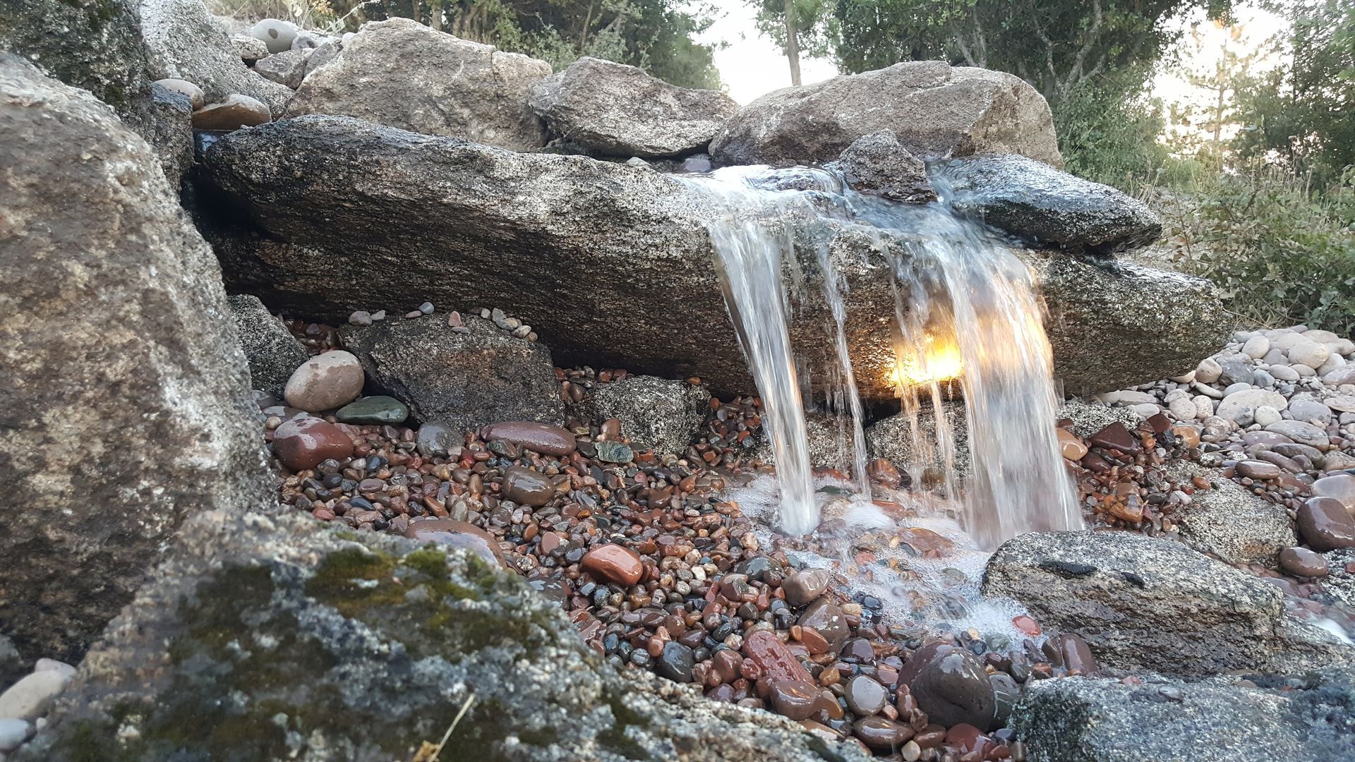 Water cascades over mossy rocks in a small waterfall feature.