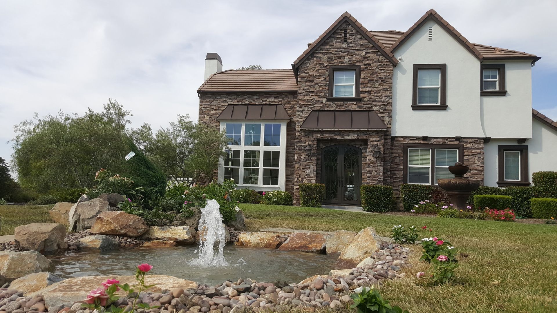 House with stone facade and fountain in front yard.