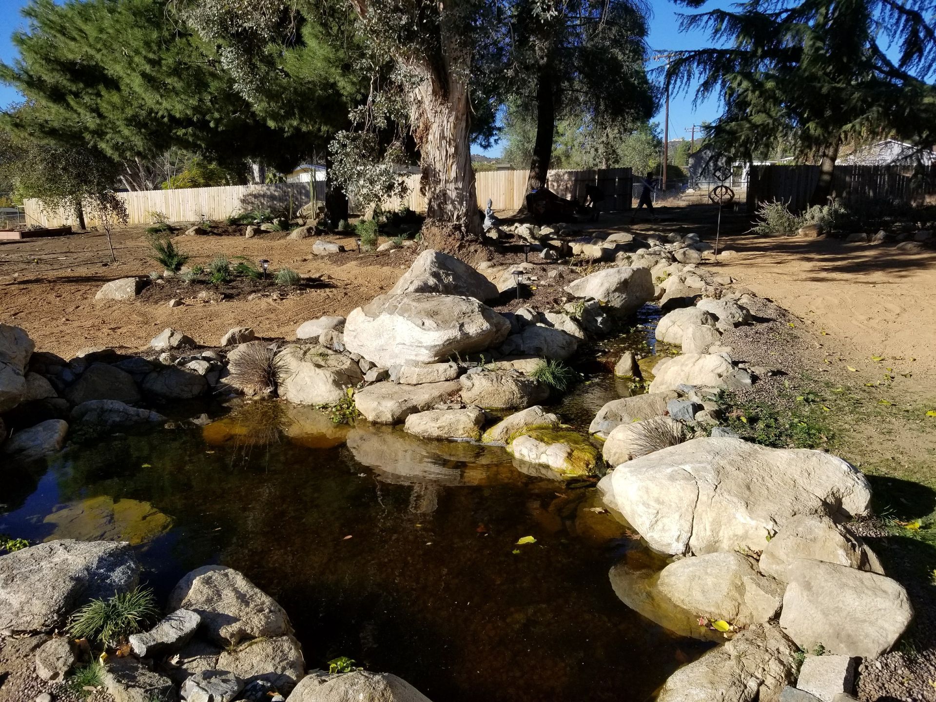 Rocky pond surrounded by stones and trees in a natural setting, with sunlight reflecting on the water.