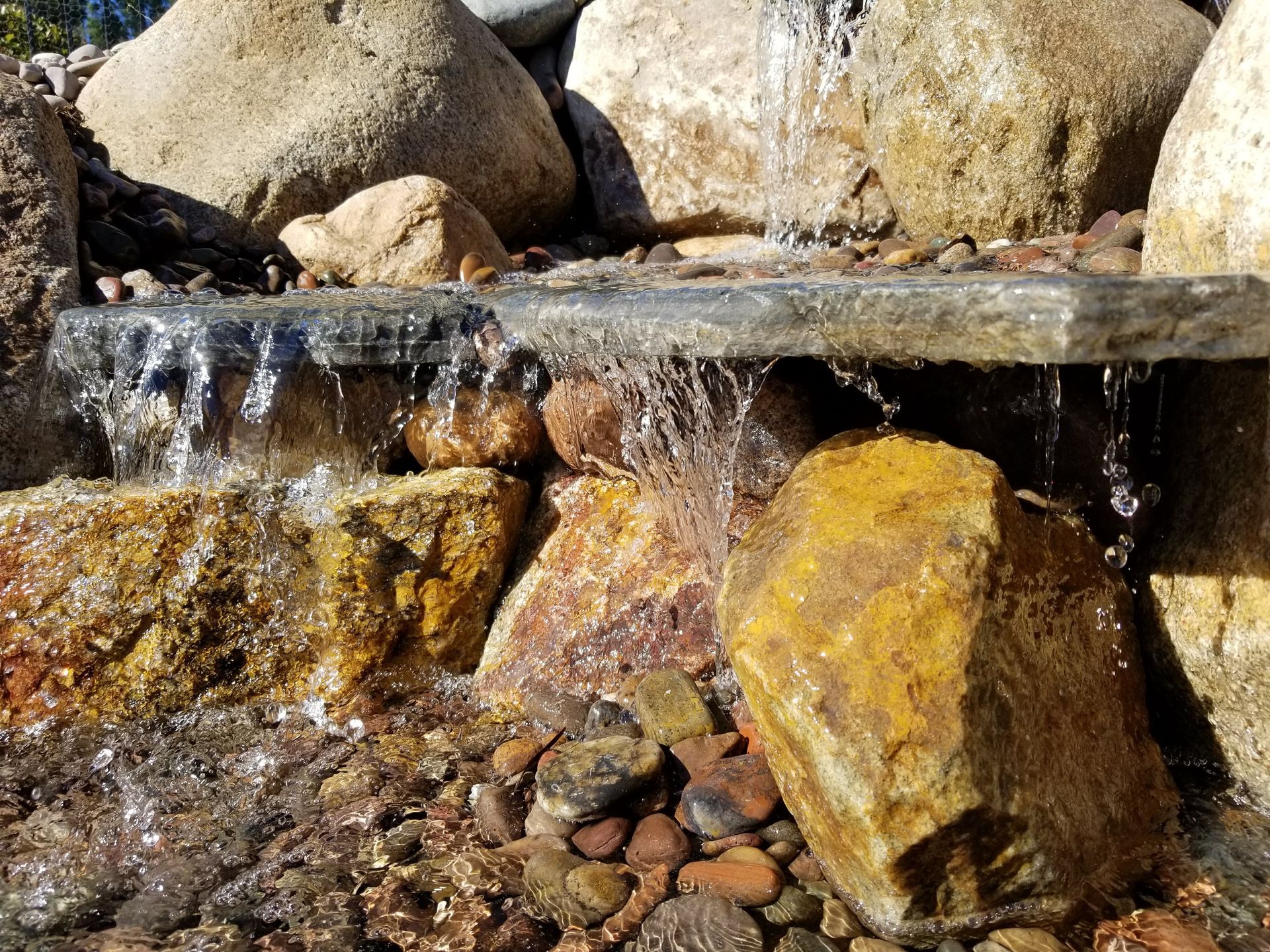 Water cascading over rocks in a naturalistic waterfall feature, with various sized stones in earthy tones.