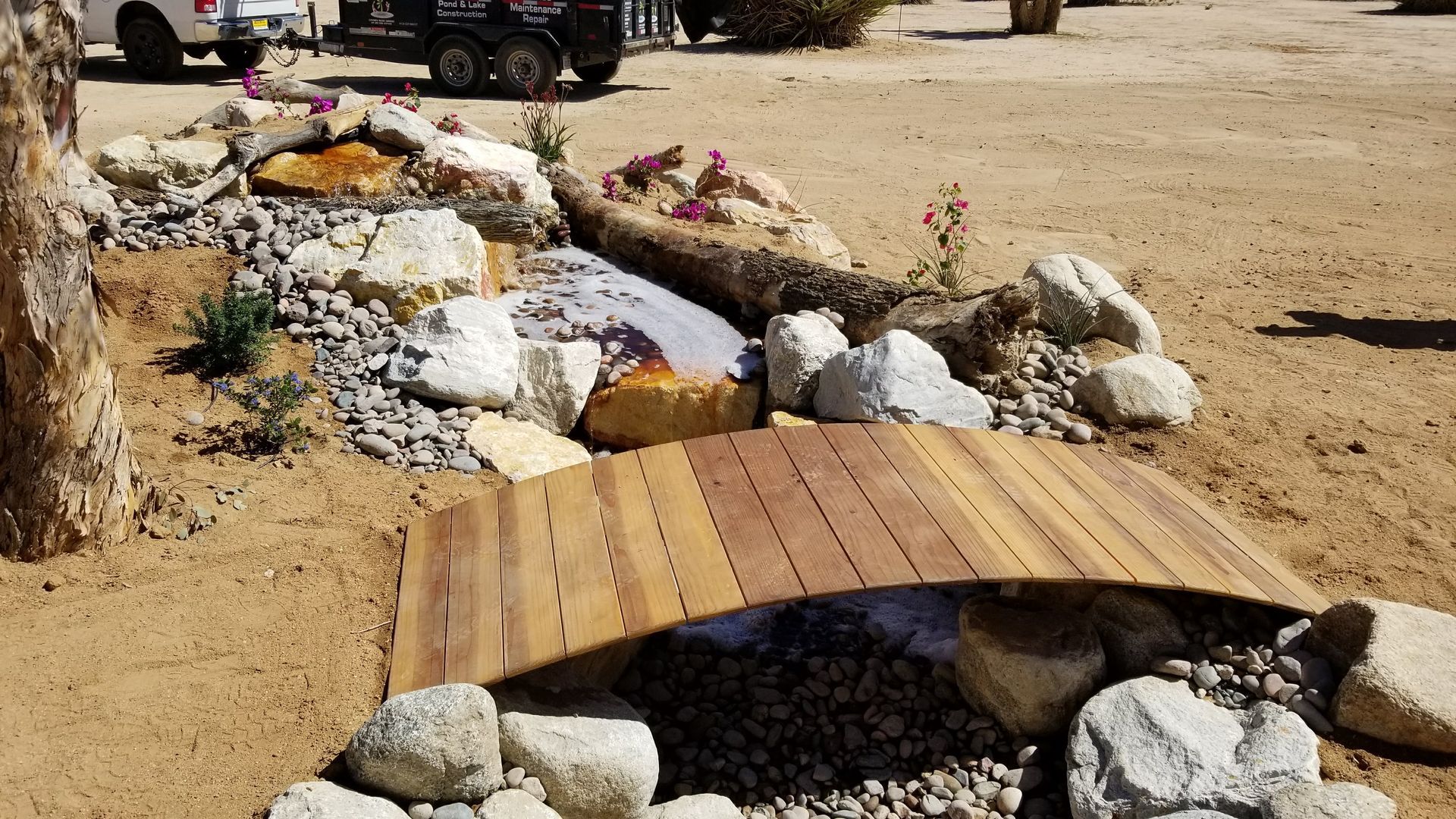 Wooden bridge over rocks and gravel in a desert landscape with sparse vegetation.