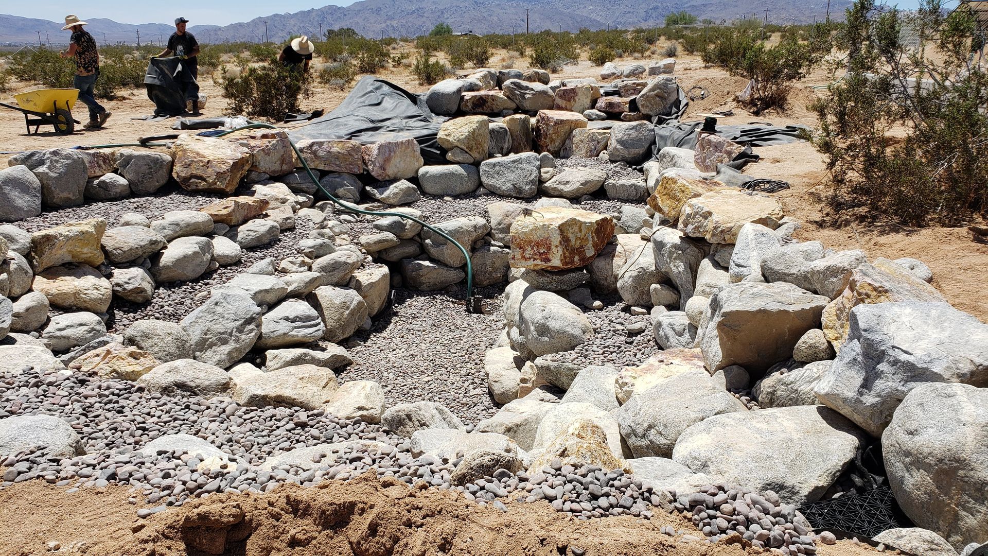 Construction site with large rocks being used to build a structure in a desert landscape.