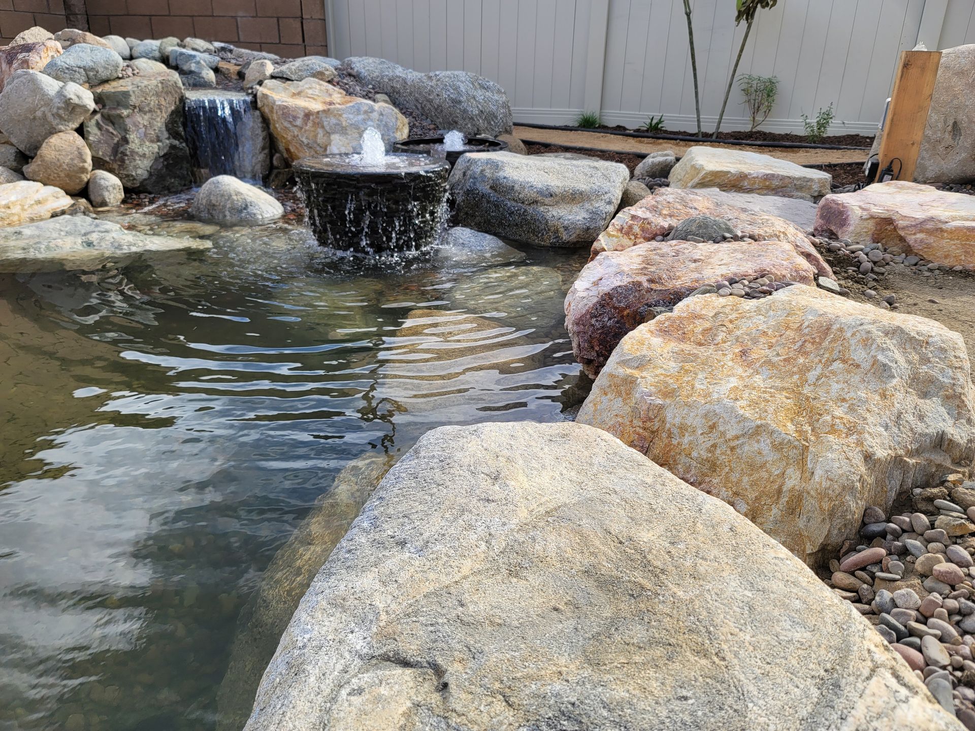 Water pond with rocks and a fountain, set in a backyard.