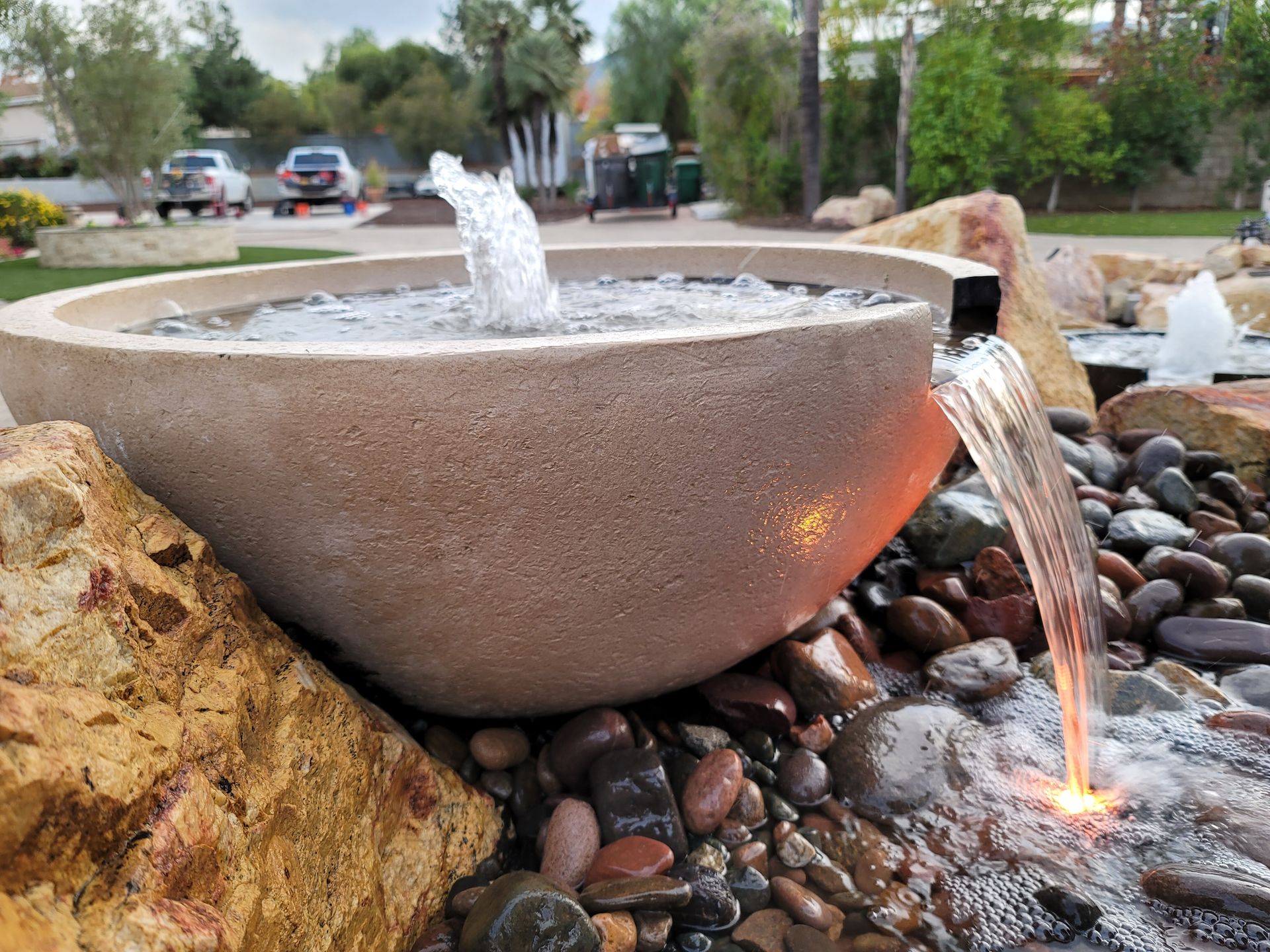 Water fountain with stone bowl, pouring water into a bed of river rocks.