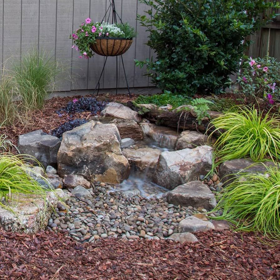 Small backyard water feature with rocks and greenery, hanging basket of flowers.