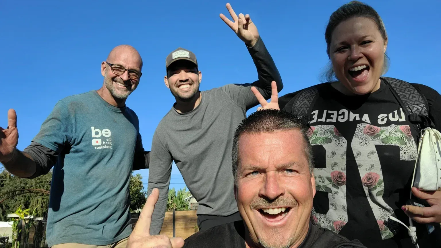 Four people smiling and making peace signs, outdoors against a blue sky.