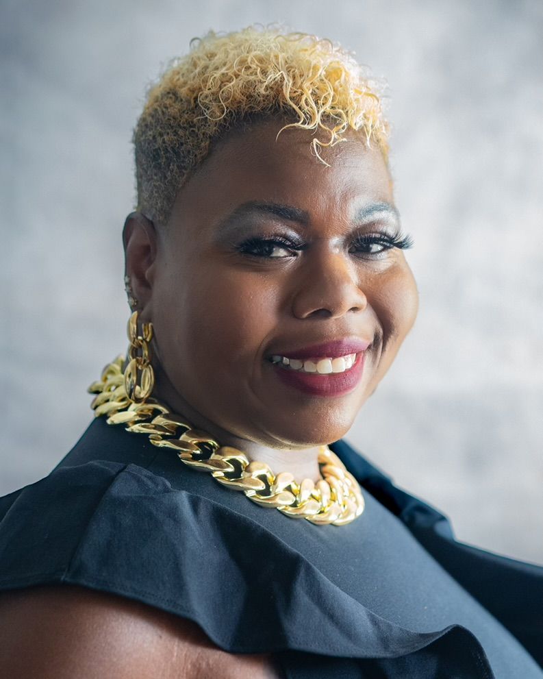 A woman wearing a gold chain necklace and earrings is smiling for the camera.