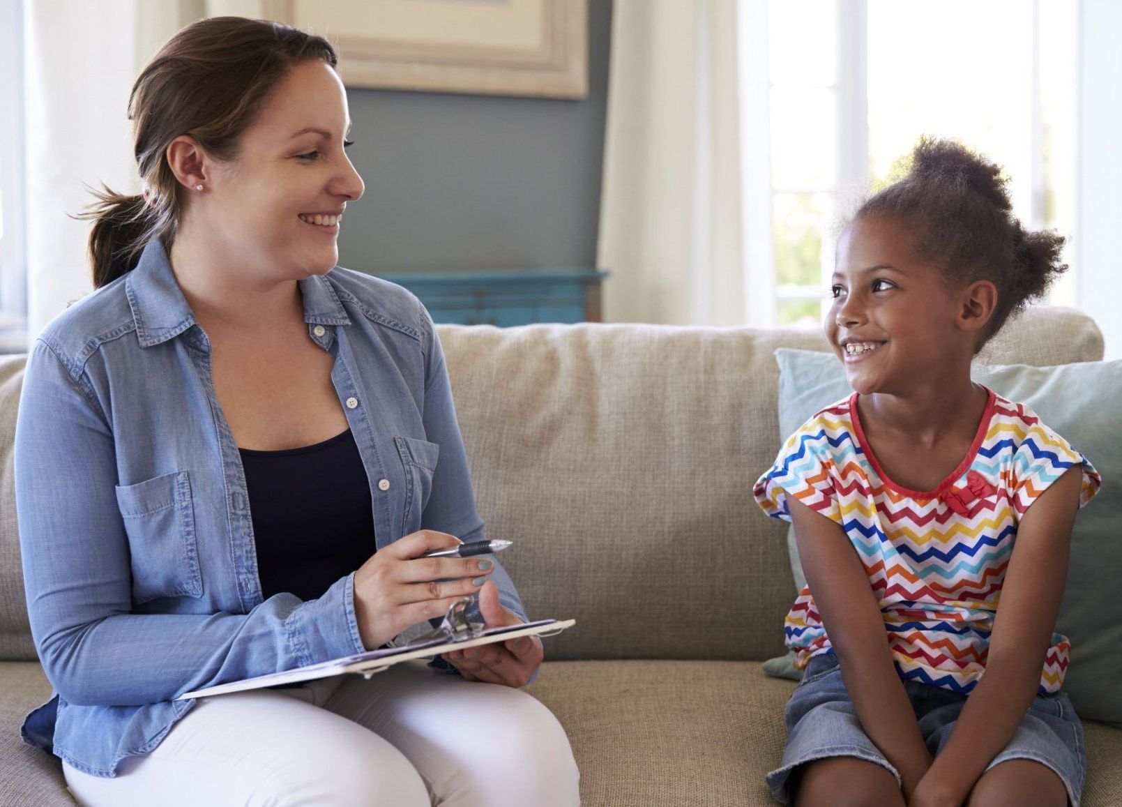 A woman is sitting on a couch talking to a little girl.