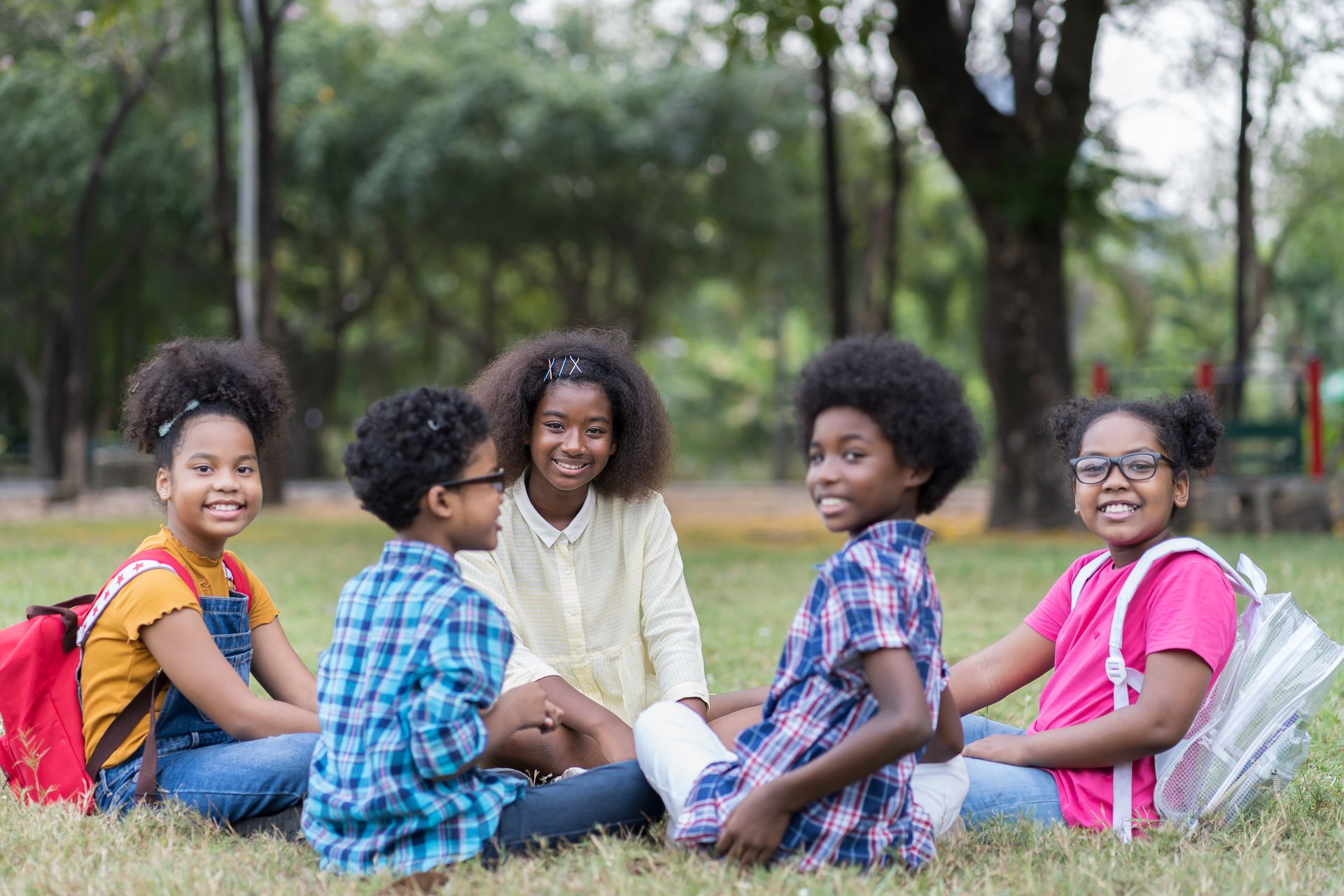 A group of children are sitting in a circle on the grass in a park.