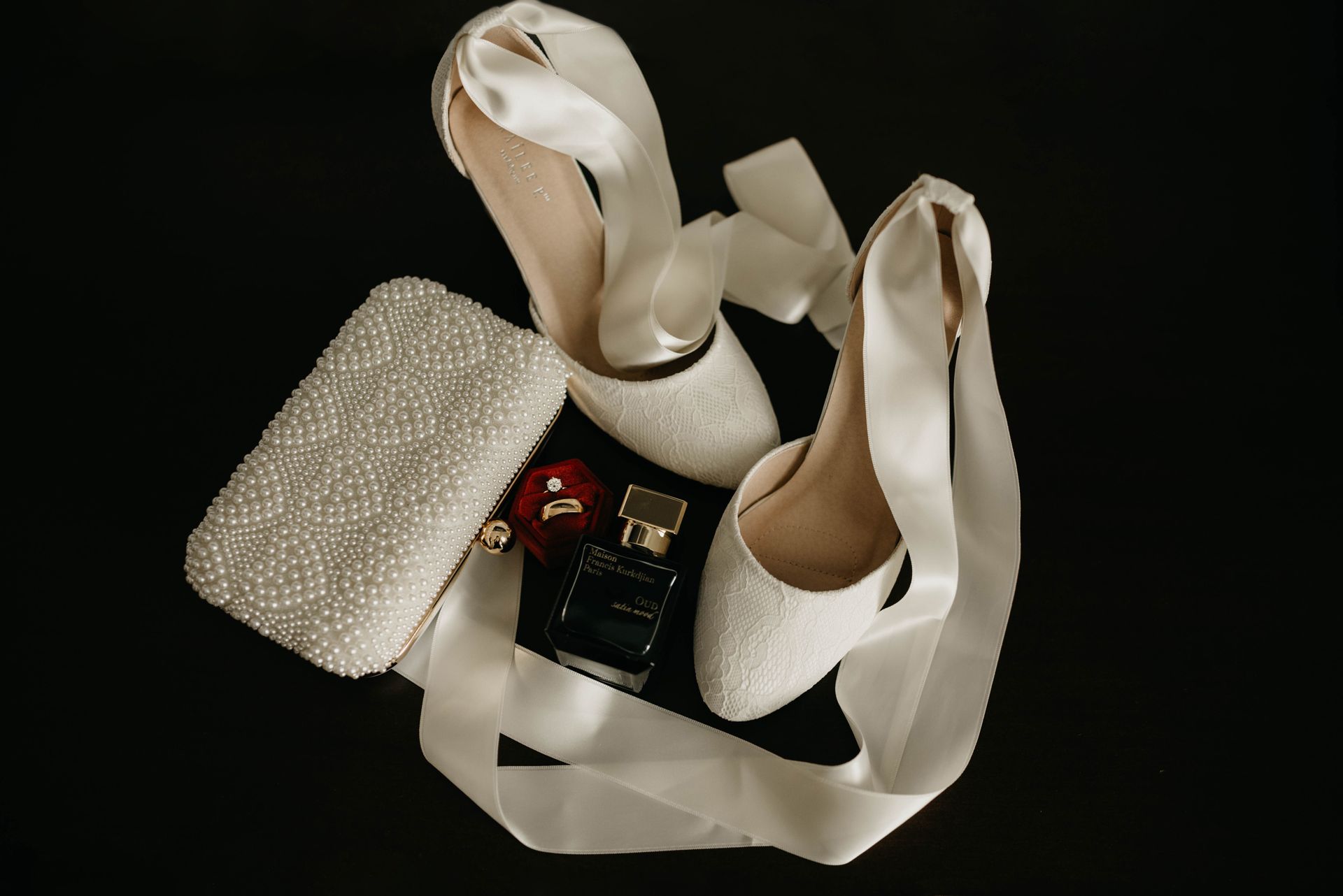 White bridal shoes and purse with perfume bottle on a black surface.
