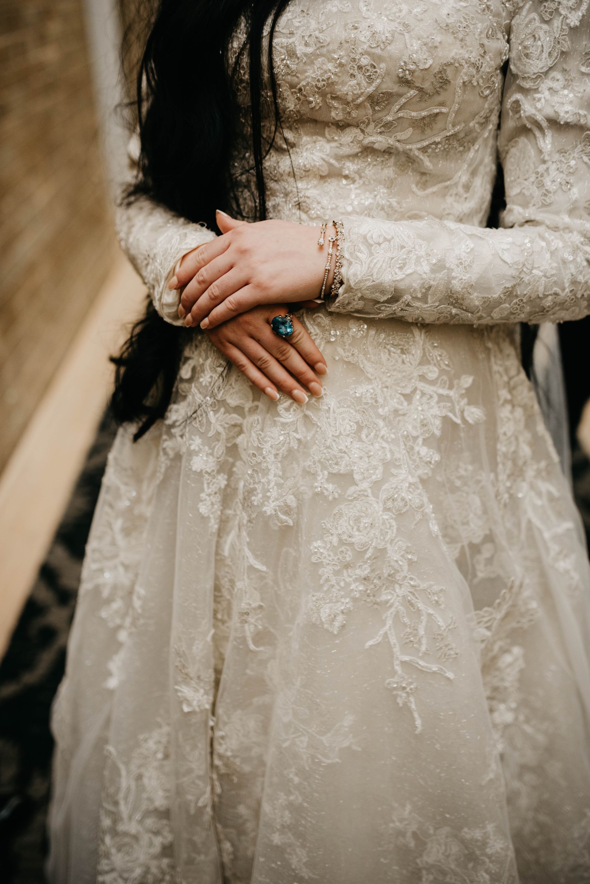 Bride in a white lace gown with long sleeves, crossed hands, wearing a turquoise ring and bracelet.