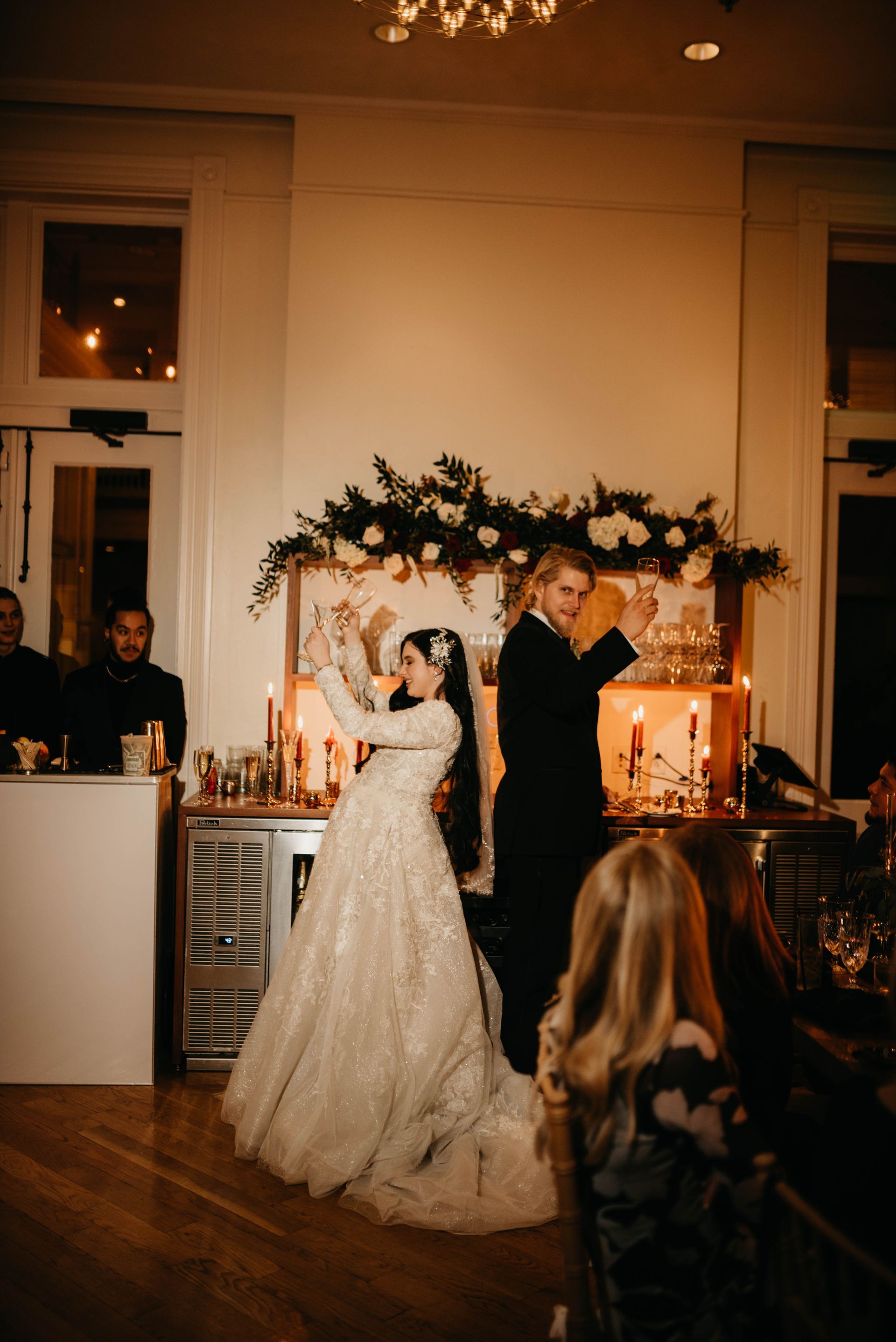 Bride and groom dance at wedding reception. Sparkling white dress, black tux, warm lighting.