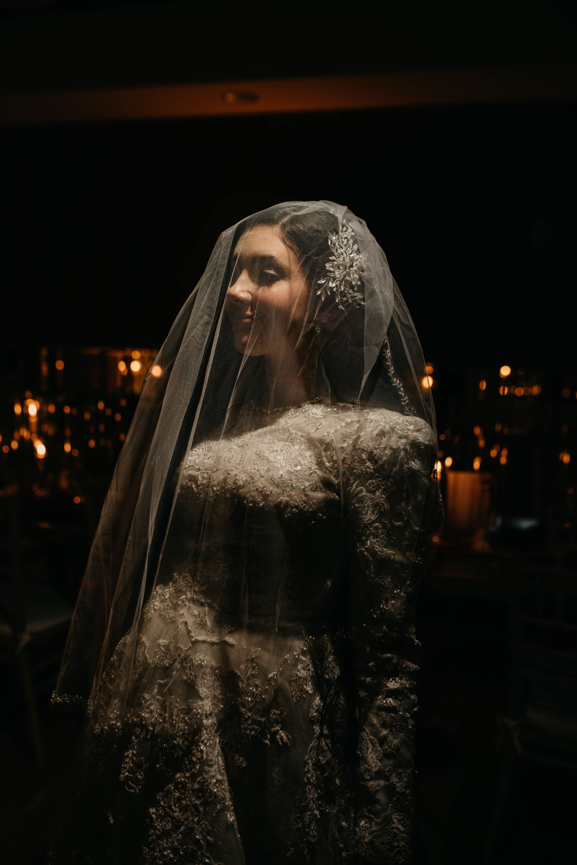 Woman in veil and gown, smiling, at a dimly lit event.