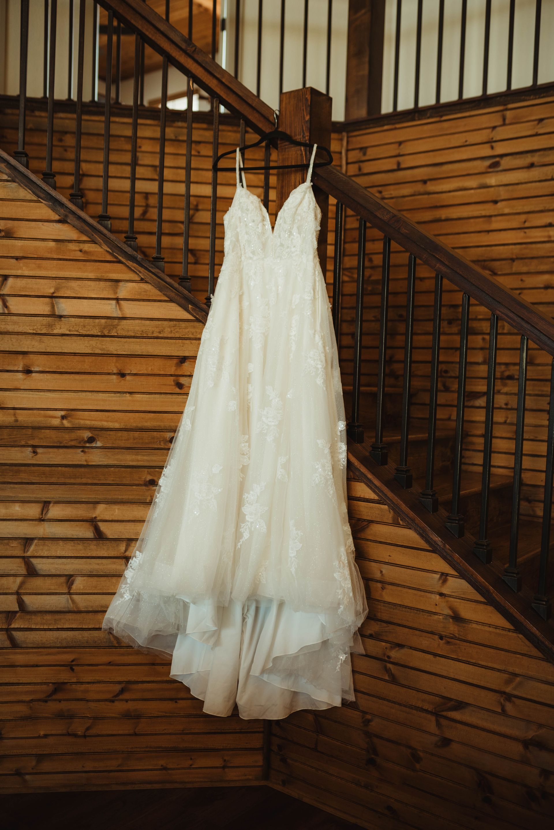 Wedding dress hanging on wooden staircase. White lace gown with spaghetti straps.