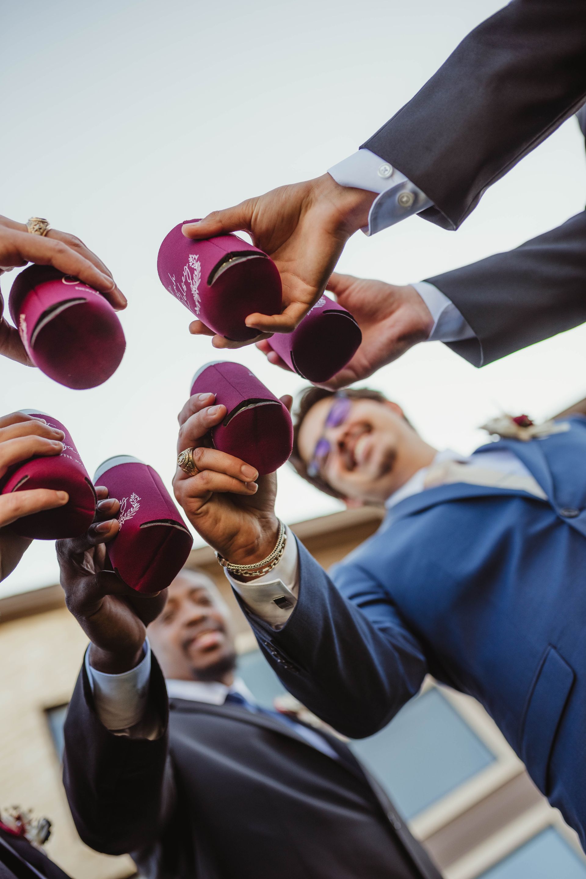 People in suits toasting with pink drink koozies, low-angle shot, outdoors.