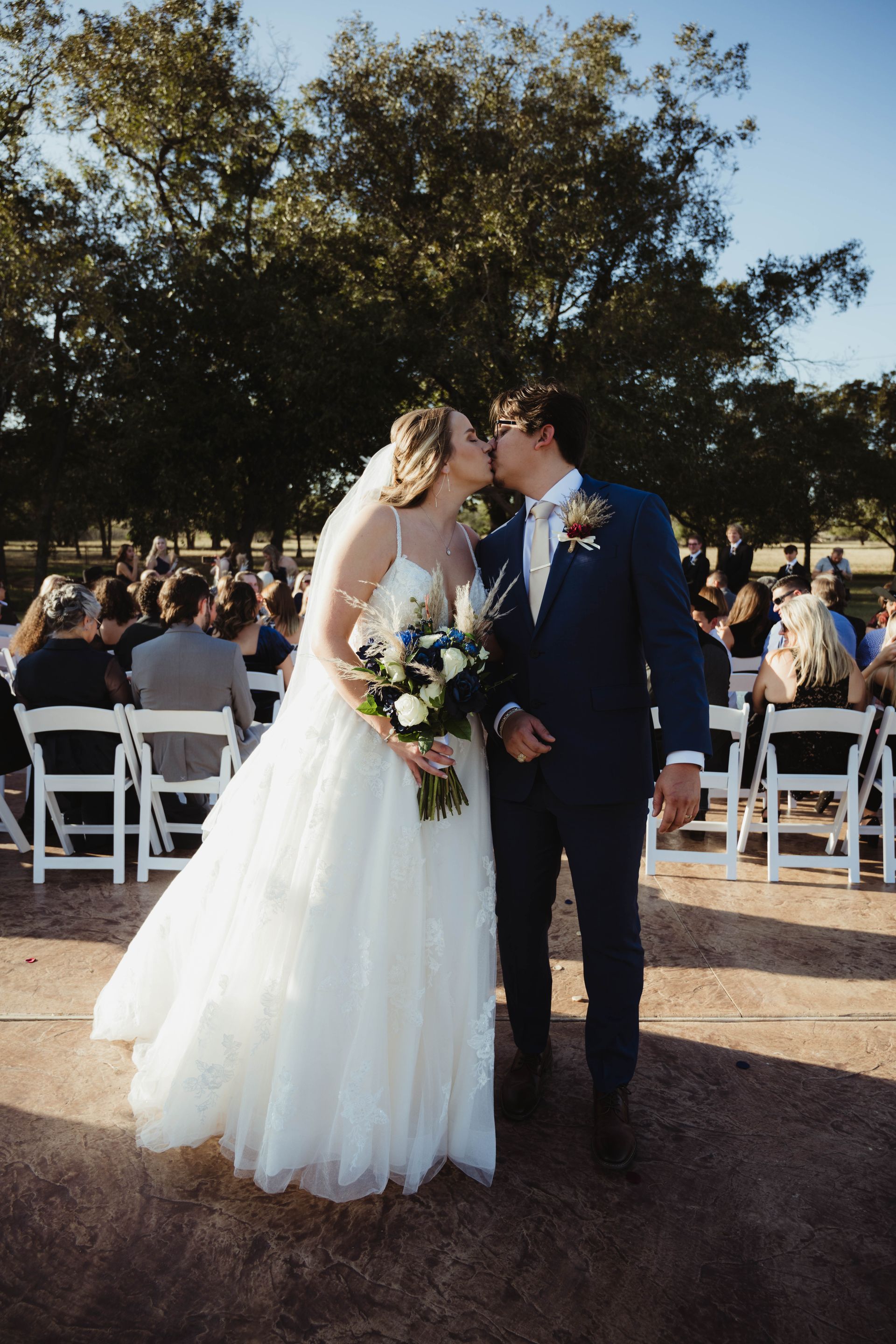 Newly married couple kissing, walking down aisle, wedding ceremony outdoors.
