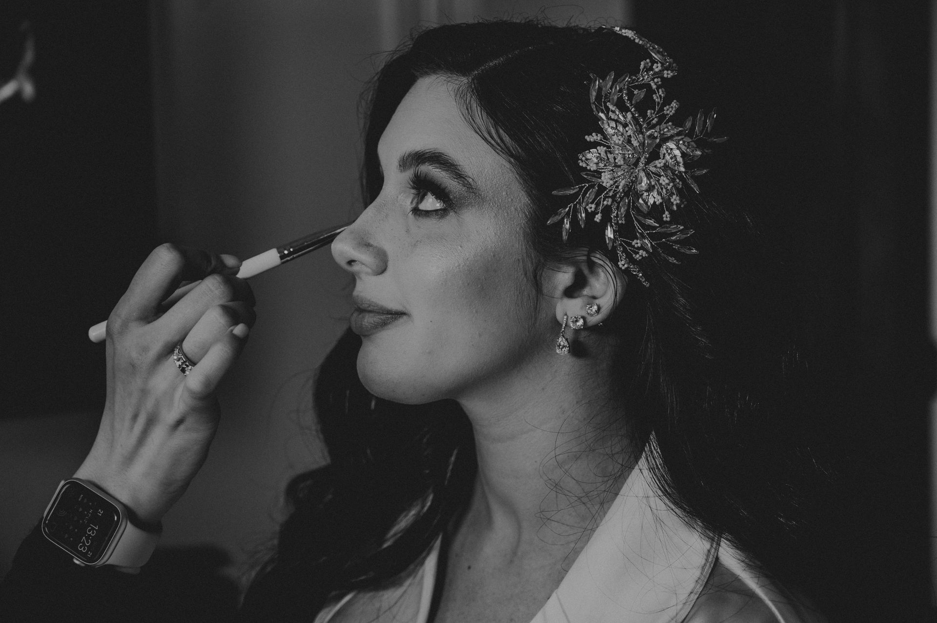 Woman getting makeup applied; wearing a floral hairpiece, in black and white.