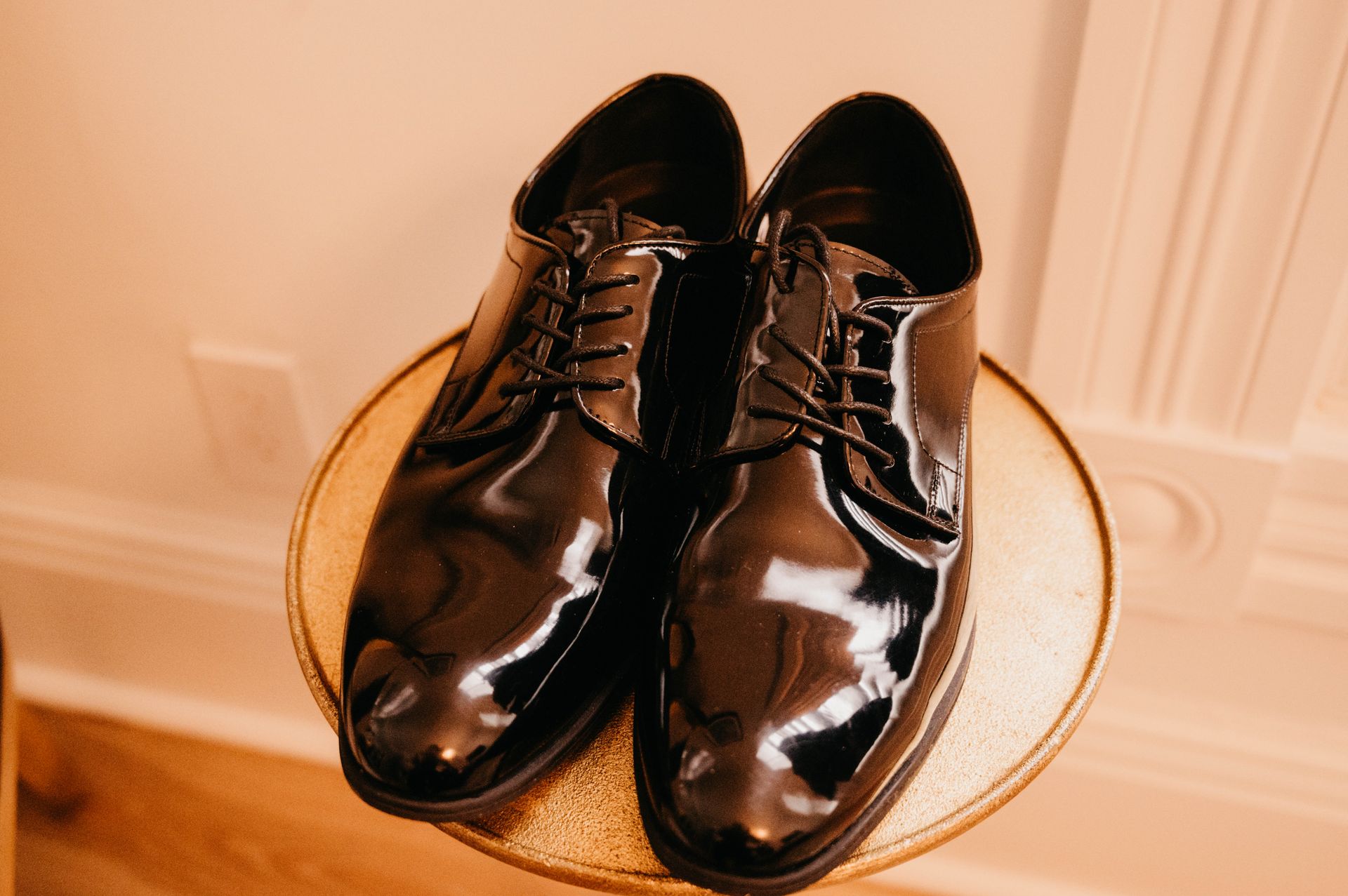 Black patent leather dress shoes on a gold round table.