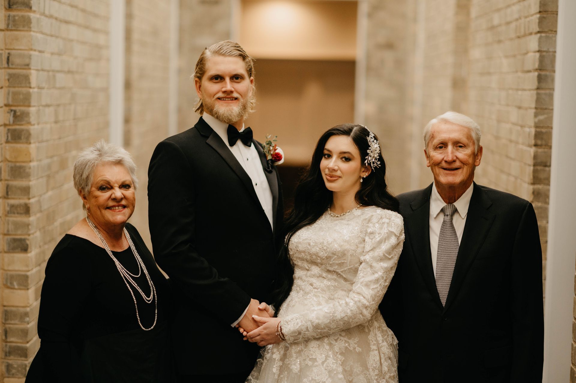 Family portrait in a hallway. Bride and groom with parents, dressed in formal attire.