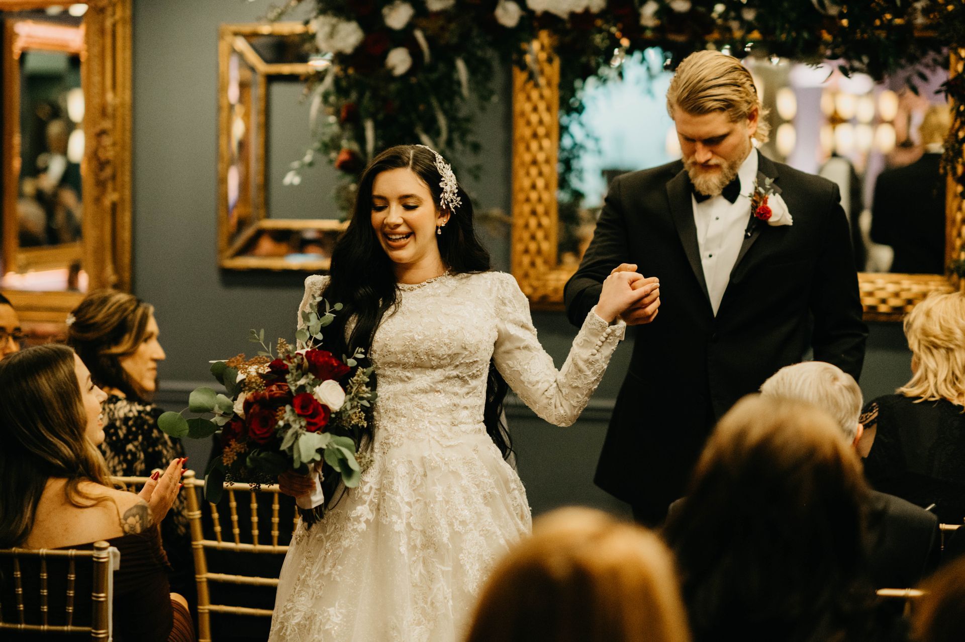 Bride and groom exit wedding ceremony, bride smiles, holding a bouquet, and groom holds her hand.