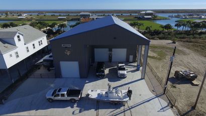 Aerial view of a large dark warehouse with parked trucks and trailers near a waterfront road.