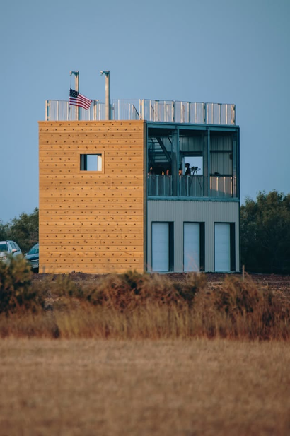 Modern two-story building with tan and blue facade in a grassy field under a clear sky