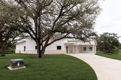 White building with large trees and a curved gravel driveway beside a green lawn.